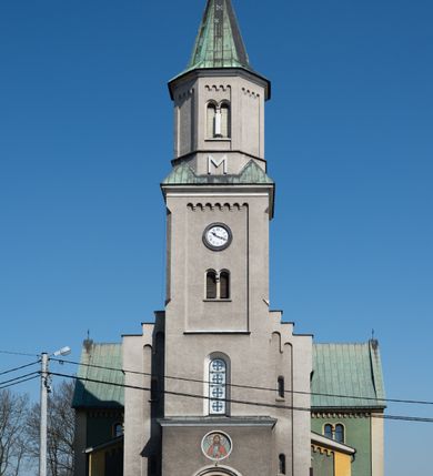 Zdjęcie nr 24: Budynki kościoła i plebanii znajdują się w centralnej części wsi, przy rynku na północ od głównej drogi z Krakowa do Oświęcimia. Kościół stoi przy obszernym placu, obwiedziony wysokim kamiennym murem z metalowym ogrodzeniem od południa. Kościół z prezbiterium zwróconym na północ, wzniesiony z kamienia wapiennego i cegły, tynkowany, z podmurówką. Świątynia wybudowana na planie krzyża łacińskiego z bazylikowym korpusem i transeptem. Dwuprzęsłowe prezbiterium zakończone półkoliście absydą zostało ujęte w dwa aneksy boczne, z których zachodni przeznaczony jest na zakrystię. Od południa do budynku przylega kruchta w przyziemiu wieży. Wnętrze kościoła trójnawowe, czteroprzęsłowe. Nawa główna łączy się z nawami bocznymi arkadami wspartymi na pięciobocznych filarach. Nawy boczne ujęte szerokimi pilastrami z pięciobocznymi filarami. Filary i pilastry stoją na wysokich, masywnych cokołach z kapitelami analogicznymi jak w nawie głównej. Ściany na skrzyżowaniu naw oraz ściany prezbiterium ujęte wspomnianymi filarami podtrzymującymi gurty sklepienia. Nawa i prezbiterium przykryte są sklepieniem kolebkowym z geometryzowanymi lunetami po obu stronach ścian. Ramiona transeptu sklepione kolebkowo z analogicznymi lunetami. Na skrzyżowaniu naw znajduje się sklepienie żaglaste. Nawę główną oświetlają rozmieszczone po jednym w każdym przęśle otwory okienne zamknięte łukiem półkolistym, okna w transepcie to biforia, widoczne tylko z zewnątrz okrągłe okno w absydzie wypełnione jest kamienną rozetą. Główne wejście od południa, do pierwszego przęsła od transeptu prowadzi dwoje drzwi w otworach o zamknięciu w kształcie łuku odciętego. W części zachodniej chór muzyczny wsparty na dwóch kolumnach i dwóch filarach dostawionych do ściany. Ich kapitele są analogiczne do pozostałych w kościele. Sklepienia dekorowane polichromią z rozetami i pękami lilii, a na skrzyżowaniu naw umieszczono malunek naścienny ukazujący Chrystusa tronującego z Bogiem Ojcem i gołębicą Ducha Świętego, a wokół nich cztery symbole ewangelistów. W fasadzie świątyni znajduje się strzelista wieża dwukondygnacyjna na planie czworokąta, przechodząca wyżej w ośmioboczną. Po bokach wieży wysokie aneksy zwieńczone schodkowo. Nad wejściem do kościoła znajduje się ozdobne okno zamknięte półkoliście i wypełnione czterema małymi rozetami ułożonymi jedna nad drugą. W kolejnej kondygnacji wieżę przepruwa biforium poniżej tarczy zegara i dekoracji arkadkowej. Wieża pełni jednocześnie funkcję dzwonnicy. Druga wieża na skrzyżowaniu nawy głównej i transeptu mieści sygnaturkę. Korpus kościoła nakryty dachem dwuspadowym, wieża wielobocznym. Wszystkie dachy kryte blachą.