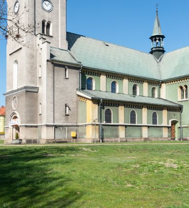Zdjęcie nr 44: Budynki kościoła i plebanii znajdują się w centralnej części wsi, przy rynku na północ od głównej drogi z Krakowa do Oświęcimia. Kościół stoi przy obszernym placu, obwiedziony wysokim kamiennym murem z metalowym ogrodzeniem od południa. Kościół z prezbiterium zwróconym na północ, wzniesiony z kamienia wapiennego i cegły, tynkowany, z podmurówką. Świątynia wybudowana na planie krzyża łacińskiego z bazylikowym korpusem i transeptem. Dwuprzęsłowe prezbiterium zakończone półkoliście absydą zostało ujęte w dwa aneksy boczne, z których zachodni przeznaczony jest na zakrystię. Od południa do budynku przylega kruchta w przyziemiu wieży. Wnętrze kościoła trójnawowe, czteroprzęsłowe. Nawa główna łączy się z nawami bocznymi arkadami wspartymi na pięciobocznych filarach. Nawy boczne ujęte szerokimi pilastrami z pięciobocznymi filarami. Filary i pilastry stoją na wysokich, masywnych cokołach z kapitelami analogicznymi jak w nawie głównej. Ściany na skrzyżowaniu naw oraz ściany prezbiterium ujęte wspomnianymi filarami podtrzymującymi gurty sklepienia. Nawa i prezbiterium przykryte są sklepieniem kolebkowym z geometryzowanymi lunetami po obu stronach ścian. Ramiona transeptu sklepione kolebkowo z analogicznymi lunetami. Na skrzyżowaniu naw znajduje się sklepienie żaglaste. Nawę główną oświetlają rozmieszczone po jednym w każdym przęśle otwory okienne zamknięte łukiem półkolistym, okna w transepcie to biforia, widoczne tylko z zewnątrz okrągłe okno w absydzie wypełnione jest kamienną rozetą. Główne wejście od południa, do pierwszego przęsła od transeptu prowadzi dwoje drzwi w otworach o zamknięciu w kształcie łuku odciętego. W części zachodniej chór muzyczny wsparty na dwóch kolumnach i dwóch filarach dostawionych do ściany. Ich kapitele są analogiczne do pozostałych w kościele. Sklepienia dekorowane polichromią z rozetami i pękami lilii, a na skrzyżowaniu naw umieszczono malunek naścienny ukazujący Chrystusa tronującego z Bogiem Ojcem i gołębicą Ducha Świętego, a wokół nich cztery symbole ewangelistów. W fasadzie świątyni znajduje się strzelista wieża dwukondygnacyjna na planie czworokąta, przechodząca wyżej w ośmioboczną. Po bokach wieży wysokie aneksy zwieńczone schodkowo. Nad wejściem do kościoła znajduje się ozdobne okno zamknięte półkoliście i wypełnione czterema małymi rozetami ułożonymi jedna nad drugą. W kolejnej kondygnacji wieżę przepruwa biforium poniżej tarczy zegara i dekoracji arkadkowej. Wieża pełni jednocześnie funkcję dzwonnicy. Druga wieża na skrzyżowaniu nawy głównej i transeptu mieści sygnaturkę. Korpus kościoła nakryty dachem dwuspadowym, wieża wielobocznym. Wszystkie dachy kryte blachą.
