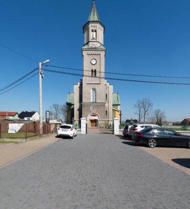 Zdjęcie nr 2: Budynki kościoła i plebanii znajdują się w centralnej części wsi, przy rynku na północ od głównej drogi z Krakowa do Oświęcimia. Kościół stoi przy obszernym placu, obwiedziony wysokim kamiennym murem z metalowym ogrodzeniem od południa. Kościół z prezbiterium zwróconym na północ, wzniesiony z kamienia wapiennego i cegły, tynkowany, z podmurówką. Świątynia wybudowana na planie krzyża łacińskiego z bazylikowym korpusem i transeptem. Dwuprzęsłowe prezbiterium zakończone półkoliście absydą zostało ujęte w dwa aneksy boczne, z których zachodni przeznaczony jest na zakrystię. Od południa do budynku przylega kruchta w przyziemiu wieży. Wnętrze kościoła trójnawowe, czteroprzęsłowe. Nawa główna łączy się z nawami bocznymi arkadami wspartymi na pięciobocznych filarach. Nawy boczne ujęte szerokimi pilastrami z pięciobocznymi filarami. Filary i pilastry stoją na wysokich, masywnych cokołach z kapitelami analogicznymi jak w nawie głównej. Ściany na skrzyżowaniu naw oraz ściany prezbiterium ujęte wspomnianymi filarami podtrzymującymi gurty sklepienia. Nawa i prezbiterium przykryte są sklepieniem kolebkowym z geometryzowanymi lunetami po obu stronach ścian. Ramiona transeptu sklepione kolebkowo z analogicznymi lunetami. Na skrzyżowaniu naw znajduje się sklepienie żaglaste. Nawę główną oświetlają rozmieszczone po jednym w każdym przęśle otwory okienne zamknięte łukiem półkolistym, okna w transepcie to biforia, widoczne tylko z zewnątrz okrągłe okno w absydzie wypełnione jest kamienną rozetą. Główne wejście od południa, do pierwszego przęsła od transeptu prowadzi dwoje drzwi w otworach o zamknięciu w kształcie łuku odciętego. W części zachodniej chór muzyczny wsparty na dwóch kolumnach i dwóch filarach dostawionych do ściany. Ich kapitele są analogiczne do pozostałych w kościele. Sklepienia dekorowane polichromią z rozetami i pękami lilii, a na skrzyżowaniu naw umieszczono malunek naścienny ukazujący Chrystusa tronującego z Bogiem Ojcem i gołębicą Ducha Świętego, a wokół nich cztery symbole ewangelistów. W fasadzie świątyni znajduje się strzelista wieża dwukondygnacyjna na planie czworokąta, przechodząca wyżej w ośmioboczną. Po bokach wieży wysokie aneksy zwieńczone schodkowo. Nad wejściem do kościoła znajduje się ozdobne okno zamknięte półkoliście i wypełnione czterema małymi rozetami ułożonymi jedna nad drugą. W kolejnej kondygnacji wieżę przepruwa biforium poniżej tarczy zegara i dekoracji arkadkowej. Wieża pełni jednocześnie funkcję dzwonnicy. Druga wieża na skrzyżowaniu nawy głównej i transeptu mieści sygnaturkę. Korpus kościoła nakryty dachem dwuspadowym, wieża wielobocznym. Wszystkie dachy kryte blachą.