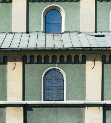 Zdjęcie nr 9: Budynki kościoła i plebanii znajdują się w centralnej części wsi, przy rynku na północ od głównej drogi z Krakowa do Oświęcimia. Kościół stoi przy obszernym placu, obwiedziony wysokim kamiennym murem z metalowym ogrodzeniem od południa. Kościół z prezbiterium zwróconym na północ, wzniesiony z kamienia wapiennego i cegły, tynkowany, z podmurówką. Świątynia wybudowana na planie krzyża łacińskiego z bazylikowym korpusem i transeptem. Dwuprzęsłowe prezbiterium zakończone półkoliście absydą zostało ujęte w dwa aneksy boczne, z których zachodni przeznaczony jest na zakrystię. Od południa do budynku przylega kruchta w przyziemiu wieży. Wnętrze kościoła trójnawowe, czteroprzęsłowe. Nawa główna łączy się z nawami bocznymi arkadami wspartymi na pięciobocznych filarach. Nawy boczne ujęte szerokimi pilastrami z pięciobocznymi filarami. Filary i pilastry stoją na wysokich, masywnych cokołach z kapitelami analogicznymi jak w nawie głównej. Ściany na skrzyżowaniu naw oraz ściany prezbiterium ujęte wspomnianymi filarami podtrzymującymi gurty sklepienia. Nawa i prezbiterium przykryte są sklepieniem kolebkowym z geometryzowanymi lunetami po obu stronach ścian. Ramiona transeptu sklepione kolebkowo z analogicznymi lunetami. Na skrzyżowaniu naw znajduje się sklepienie żaglaste. Nawę główną oświetlają rozmieszczone po jednym w każdym przęśle otwory okienne zamknięte łukiem półkolistym, okna w transepcie to biforia, widoczne tylko z zewnątrz okrągłe okno w absydzie wypełnione jest kamienną rozetą. Główne wejście od południa, do pierwszego przęsła od transeptu prowadzi dwoje drzwi w otworach o zamknięciu w kształcie łuku odciętego. W części zachodniej chór muzyczny wsparty na dwóch kolumnach i dwóch filarach dostawionych do ściany. Ich kapitele są analogiczne do pozostałych w kościele. Sklepienia dekorowane polichromią z rozetami i pękami lilii, a na skrzyżowaniu naw umieszczono malunek naścienny ukazujący Chrystusa tronującego z Bogiem Ojcem i gołębicą Ducha Świętego, a wokół nich cztery symbole ewangelistów. W fasadzie świątyni znajduje się strzelista wieża dwukondygnacyjna na planie czworokąta, przechodząca wyżej w ośmioboczną. Po bokach wieży wysokie aneksy zwieńczone schodkowo. Nad wejściem do kościoła znajduje się ozdobne okno zamknięte półkoliście i wypełnione czterema małymi rozetami ułożonymi jedna nad drugą. W kolejnej kondygnacji wieżę przepruwa biforium poniżej tarczy zegara i dekoracji arkadkowej. Wieża pełni jednocześnie funkcję dzwonnicy. Druga wieża na skrzyżowaniu nawy głównej i transeptu mieści sygnaturkę. Korpus kościoła nakryty dachem dwuspadowym, wieża wielobocznym. Wszystkie dachy kryte blachą.