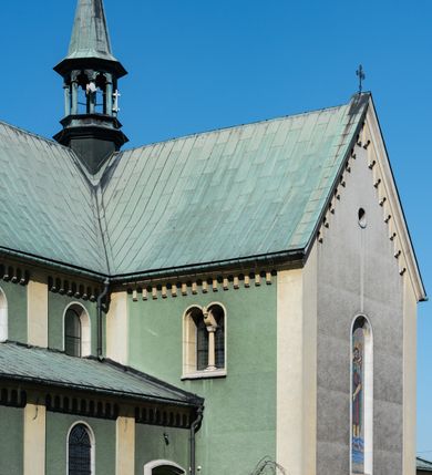 Zdjęcie nr 6: Budynki kościoła i plebanii znajdują się w centralnej części wsi, przy rynku na północ od głównej drogi z Krakowa do Oświęcimia. Kościół stoi przy obszernym placu, obwiedziony wysokim kamiennym murem z metalowym ogrodzeniem od południa. Kościół z prezbiterium zwróconym na północ, wzniesiony z kamienia wapiennego i cegły, tynkowany, z podmurówką. Świątynia wybudowana na planie krzyża łacińskiego z bazylikowym korpusem i transeptem. Dwuprzęsłowe prezbiterium zakończone półkoliście absydą zostało ujęte w dwa aneksy boczne, z których zachodni przeznaczony jest na zakrystię. Od południa do budynku przylega kruchta w przyziemiu wieży. Wnętrze kościoła trójnawowe, czteroprzęsłowe. Nawa główna łączy się z nawami bocznymi arkadami wspartymi na pięciobocznych filarach. Nawy boczne ujęte szerokimi pilastrami z pięciobocznymi filarami. Filary i pilastry stoją na wysokich, masywnych cokołach z kapitelami analogicznymi jak w nawie głównej. Ściany na skrzyżowaniu naw oraz ściany prezbiterium ujęte wspomnianymi filarami podtrzymującymi gurty sklepienia. Nawa i prezbiterium przykryte są sklepieniem kolebkowym z geometryzowanymi lunetami po obu stronach ścian. Ramiona transeptu sklepione kolebkowo z analogicznymi lunetami. Na skrzyżowaniu naw znajduje się sklepienie żaglaste. Nawę główną oświetlają rozmieszczone po jednym w każdym przęśle otwory okienne zamknięte łukiem półkolistym, okna w transepcie to biforia, widoczne tylko z zewnątrz okrągłe okno w absydzie wypełnione jest kamienną rozetą. Główne wejście od południa, do pierwszego przęsła od transeptu prowadzi dwoje drzwi w otworach o zamknięciu w kształcie łuku odciętego. W części zachodniej chór muzyczny wsparty na dwóch kolumnach i dwóch filarach dostawionych do ściany. Ich kapitele są analogiczne do pozostałych w kościele. Sklepienia dekorowane polichromią z rozetami i pękami lilii, a na skrzyżowaniu naw umieszczono malunek naścienny ukazujący Chrystusa tronującego z Bogiem Ojcem i gołębicą Ducha Świętego, a wokół nich cztery symbole ewangelistów. W fasadzie świątyni znajduje się strzelista wieża dwukondygnacyjna na planie czworokąta, przechodząca wyżej w ośmioboczną. Po bokach wieży wysokie aneksy zwieńczone schodkowo. Nad wejściem do kościoła znajduje się ozdobne okno zamknięte półkoliście i wypełnione czterema małymi rozetami ułożonymi jedna nad drugą. W kolejnej kondygnacji wieżę przepruwa biforium poniżej tarczy zegara i dekoracji arkadkowej. Wieża pełni jednocześnie funkcję dzwonnicy. Druga wieża na skrzyżowaniu nawy głównej i transeptu mieści sygnaturkę. Korpus kościoła nakryty dachem dwuspadowym, wieża wielobocznym. Wszystkie dachy kryte blachą.