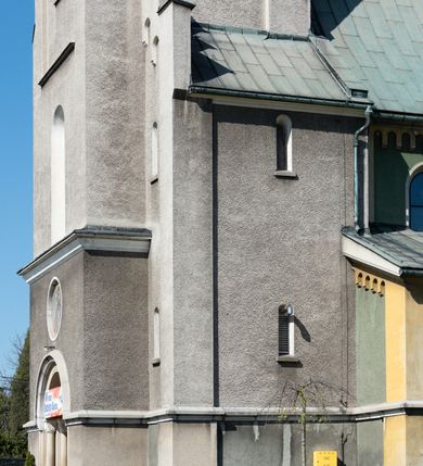 Zdjęcie nr 45: Budynki kościoła i plebanii znajdują się w centralnej części wsi, przy rynku na północ od głównej drogi z Krakowa do Oświęcimia. Kościół stoi przy obszernym placu, obwiedziony wysokim kamiennym murem z metalowym ogrodzeniem od południa. Kościół z prezbiterium zwróconym na północ, wzniesiony z kamienia wapiennego i cegły, tynkowany, z podmurówką. Świątynia wybudowana na planie krzyża łacińskiego z bazylikowym korpusem i transeptem. Dwuprzęsłowe prezbiterium zakończone półkoliście absydą zostało ujęte w dwa aneksy boczne, z których zachodni przeznaczony jest na zakrystię. Od południa do budynku przylega kruchta w przyziemiu wieży. Wnętrze kościoła trójnawowe, czteroprzęsłowe. Nawa główna łączy się z nawami bocznymi arkadami wspartymi na pięciobocznych filarach. Nawy boczne ujęte szerokimi pilastrami z pięciobocznymi filarami. Filary i pilastry stoją na wysokich, masywnych cokołach z kapitelami analogicznymi jak w nawie głównej. Ściany na skrzyżowaniu naw oraz ściany prezbiterium ujęte wspomnianymi filarami podtrzymującymi gurty sklepienia. Nawa i prezbiterium przykryte są sklepieniem kolebkowym z geometryzowanymi lunetami po obu stronach ścian. Ramiona transeptu sklepione kolebkowo z analogicznymi lunetami. Na skrzyżowaniu naw znajduje się sklepienie żaglaste. Nawę główną oświetlają rozmieszczone po jednym w każdym przęśle otwory okienne zamknięte łukiem półkolistym, okna w transepcie to biforia, widoczne tylko z zewnątrz okrągłe okno w absydzie wypełnione jest kamienną rozetą. Główne wejście od południa, do pierwszego przęsła od transeptu prowadzi dwoje drzwi w otworach o zamknięciu w kształcie łuku odciętego. W części zachodniej chór muzyczny wsparty na dwóch kolumnach i dwóch filarach dostawionych do ściany. Ich kapitele są analogiczne do pozostałych w kościele. Sklepienia dekorowane polichromią z rozetami i pękami lilii, a na skrzyżowaniu naw umieszczono malunek naścienny ukazujący Chrystusa tronującego z Bogiem Ojcem i gołębicą Ducha Świętego, a wokół nich cztery symbole ewangelistów. W fasadzie świątyni znajduje się strzelista wieża dwukondygnacyjna na planie czworokąta, przechodząca wyżej w ośmioboczną. Po bokach wieży wysokie aneksy zwieńczone schodkowo. Nad wejściem do kościoła znajduje się ozdobne okno zamknięte półkoliście i wypełnione czterema małymi rozetami ułożonymi jedna nad drugą. W kolejnej kondygnacji wieżę przepruwa biforium poniżej tarczy zegara i dekoracji arkadkowej. Wieża pełni jednocześnie funkcję dzwonnicy. Druga wieża na skrzyżowaniu nawy głównej i transeptu mieści sygnaturkę. Korpus kościoła nakryty dachem dwuspadowym, wieża wielobocznym. Wszystkie dachy kryte blachą.