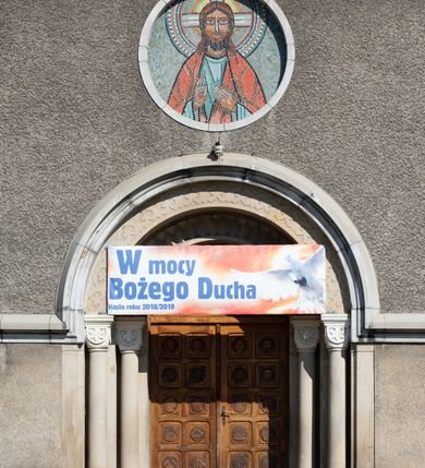 Zdjęcie nr 21: Budynki kościoła i plebanii znajdują się w centralnej części wsi, przy rynku na północ od głównej drogi z Krakowa do Oświęcimia. Kościół stoi przy obszernym placu, obwiedziony wysokim kamiennym murem z metalowym ogrodzeniem od południa. Kościół z prezbiterium zwróconym na północ, wzniesiony z kamienia wapiennego i cegły, tynkowany, z podmurówką. Świątynia wybudowana na planie krzyża łacińskiego z bazylikowym korpusem i transeptem. Dwuprzęsłowe prezbiterium zakończone półkoliście absydą zostało ujęte w dwa aneksy boczne, z których zachodni przeznaczony jest na zakrystię. Od południa do budynku przylega kruchta w przyziemiu wieży. Wnętrze kościoła trójnawowe, czteroprzęsłowe. Nawa główna łączy się z nawami bocznymi arkadami wspartymi na pięciobocznych filarach. Nawy boczne ujęte szerokimi pilastrami z pięciobocznymi filarami. Filary i pilastry stoją na wysokich, masywnych cokołach z kapitelami analogicznymi jak w nawie głównej. Ściany na skrzyżowaniu naw oraz ściany prezbiterium ujęte wspomnianymi filarami podtrzymującymi gurty sklepienia. Nawa i prezbiterium przykryte są sklepieniem kolebkowym z geometryzowanymi lunetami po obu stronach ścian. Ramiona transeptu sklepione kolebkowo z analogicznymi lunetami. Na skrzyżowaniu naw znajduje się sklepienie żaglaste. Nawę główną oświetlają rozmieszczone po jednym w każdym przęśle otwory okienne zamknięte łukiem półkolistym, okna w transepcie to biforia, widoczne tylko z zewnątrz okrągłe okno w absydzie wypełnione jest kamienną rozetą. Główne wejście od południa, do pierwszego przęsła od transeptu prowadzi dwoje drzwi w otworach o zamknięciu w kształcie łuku odciętego. W części zachodniej chór muzyczny wsparty na dwóch kolumnach i dwóch filarach dostawionych do ściany. Ich kapitele są analogiczne do pozostałych w kościele. Sklepienia dekorowane polichromią z rozetami i pękami lilii, a na skrzyżowaniu naw umieszczono malunek naścienny ukazujący Chrystusa tronującego z Bogiem Ojcem i gołębicą Ducha Świętego, a wokół nich cztery symbole ewangelistów. W fasadzie świątyni znajduje się strzelista wieża dwukondygnacyjna na planie czworokąta, przechodząca wyżej w ośmioboczną. Po bokach wieży wysokie aneksy zwieńczone schodkowo. Nad wejściem do kościoła znajduje się ozdobne okno zamknięte półkoliście i wypełnione czterema małymi rozetami ułożonymi jedna nad drugą. W kolejnej kondygnacji wieżę przepruwa biforium poniżej tarczy zegara i dekoracji arkadkowej. Wieża pełni jednocześnie funkcję dzwonnicy. Druga wieża na skrzyżowaniu nawy głównej i transeptu mieści sygnaturkę. Korpus kościoła nakryty dachem dwuspadowym, wieża wielobocznym. Wszystkie dachy kryte blachą.