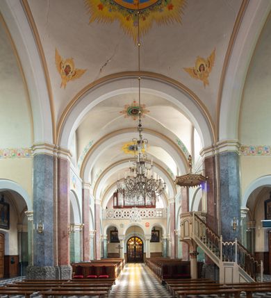 Zdjęcie nr 38: Budynki kościoła i plebanii znajdują się w centralnej części wsi, przy rynku na północ od głównej drogi z Krakowa do Oświęcimia. Kościół stoi przy obszernym placu, obwiedziony wysokim kamiennym murem z metalowym ogrodzeniem od południa. Kościół z prezbiterium zwróconym na północ, wzniesiony z kamienia wapiennego i cegły, tynkowany, z podmurówką. Świątynia wybudowana na planie krzyża łacińskiego z bazylikowym korpusem i transeptem. Dwuprzęsłowe prezbiterium zakończone półkoliście absydą zostało ujęte w dwa aneksy boczne, z których zachodni przeznaczony jest na zakrystię. Od południa do budynku przylega kruchta w przyziemiu wieży. Wnętrze kościoła trójnawowe, czteroprzęsłowe. Nawa główna łączy się z nawami bocznymi arkadami wspartymi na pięciobocznych filarach. Nawy boczne ujęte szerokimi pilastrami z pięciobocznymi filarami. Filary i pilastry stoją na wysokich, masywnych cokołach z kapitelami analogicznymi jak w nawie głównej. Ściany na skrzyżowaniu naw oraz ściany prezbiterium ujęte wspomnianymi filarami podtrzymującymi gurty sklepienia. Nawa i prezbiterium przykryte są sklepieniem kolebkowym z geometryzowanymi lunetami po obu stronach ścian. Ramiona transeptu sklepione kolebkowo z analogicznymi lunetami. Na skrzyżowaniu naw znajduje się sklepienie żaglaste. Nawę główną oświetlają rozmieszczone po jednym w każdym przęśle otwory okienne zamknięte łukiem półkolistym, okna w transepcie to biforia, widoczne tylko z zewnątrz okrągłe okno w absydzie wypełnione jest kamienną rozetą. Główne wejście od południa, do pierwszego przęsła od transeptu prowadzi dwoje drzwi w otworach o zamknięciu w kształcie łuku odciętego. W części zachodniej chór muzyczny wsparty na dwóch kolumnach i dwóch filarach dostawionych do ściany. Ich kapitele są analogiczne do pozostałych w kościele. Sklepienia dekorowane polichromią z rozetami i pękami lilii, a na skrzyżowaniu naw umieszczono malunek naścienny ukazujący Chrystusa tronującego z Bogiem Ojcem i gołębicą Ducha Świętego, a wokół nich cztery symbole ewangelistów. W fasadzie świątyni znajduje się strzelista wieża dwukondygnacyjna na planie czworokąta, przechodząca wyżej w ośmioboczną. Po bokach wieży wysokie aneksy zwieńczone schodkowo. Nad wejściem do kościoła znajduje się ozdobne okno zamknięte półkoliście i wypełnione czterema małymi rozetami ułożonymi jedna nad drugą. W kolejnej kondygnacji wieżę przepruwa biforium poniżej tarczy zegara i dekoracji arkadkowej. Wieża pełni jednocześnie funkcję dzwonnicy. Druga wieża na skrzyżowaniu nawy głównej i transeptu mieści sygnaturkę. Korpus kościoła nakryty dachem dwuspadowym, wieża wielobocznym. Wszystkie dachy kryte blachą.