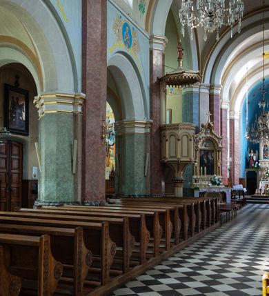 Zdjęcie nr 33: Budynki kościoła i plebanii znajdują się w centralnej części wsi, przy rynku na północ od głównej drogi z Krakowa do Oświęcimia. Kościół stoi przy obszernym placu, obwiedziony wysokim kamiennym murem z metalowym ogrodzeniem od południa. Kościół z prezbiterium zwróconym na północ, wzniesiony z kamienia wapiennego i cegły, tynkowany, z podmurówką. Świątynia wybudowana na planie krzyża łacińskiego z bazylikowym korpusem i transeptem. Dwuprzęsłowe prezbiterium zakończone półkoliście absydą zostało ujęte w dwa aneksy boczne, z których zachodni przeznaczony jest na zakrystię. Od południa do budynku przylega kruchta w przyziemiu wieży. Wnętrze kościoła trójnawowe, czteroprzęsłowe. Nawa główna łączy się z nawami bocznymi arkadami wspartymi na pięciobocznych filarach. Nawy boczne ujęte szerokimi pilastrami z pięciobocznymi filarami. Filary i pilastry stoją na wysokich, masywnych cokołach z kapitelami analogicznymi jak w nawie głównej. Ściany na skrzyżowaniu naw oraz ściany prezbiterium ujęte wspomnianymi filarami podtrzymującymi gurty sklepienia. Nawa i prezbiterium przykryte są sklepieniem kolebkowym z geometryzowanymi lunetami po obu stronach ścian. Ramiona transeptu sklepione kolebkowo z analogicznymi lunetami. Na skrzyżowaniu naw znajduje się sklepienie żaglaste. Nawę główną oświetlają rozmieszczone po jednym w każdym przęśle otwory okienne zamknięte łukiem półkolistym, okna w transepcie to biforia, widoczne tylko z zewnątrz okrągłe okno w absydzie wypełnione jest kamienną rozetą. Główne wejście od południa, do pierwszego przęsła od transeptu prowadzi dwoje drzwi w otworach o zamknięciu w kształcie łuku odciętego. W części zachodniej chór muzyczny wsparty na dwóch kolumnach i dwóch filarach dostawionych do ściany. Ich kapitele są analogiczne do pozostałych w kościele. Sklepienia dekorowane polichromią z rozetami i pękami lilii, a na skrzyżowaniu naw umieszczono malunek naścienny ukazujący Chrystusa tronującego z Bogiem Ojcem i gołębicą Ducha Świętego, a wokół nich cztery symbole ewangelistów. W fasadzie świątyni znajduje się strzelista wieża dwukondygnacyjna na planie czworokąta, przechodząca wyżej w ośmioboczną. Po bokach wieży wysokie aneksy zwieńczone schodkowo. Nad wejściem do kościoła znajduje się ozdobne okno zamknięte półkoliście i wypełnione czterema małymi rozetami ułożonymi jedna nad drugą. W kolejnej kondygnacji wieżę przepruwa biforium poniżej tarczy zegara i dekoracji arkadkowej. Wieża pełni jednocześnie funkcję dzwonnicy. Druga wieża na skrzyżowaniu nawy głównej i transeptu mieści sygnaturkę. Korpus kościoła nakryty dachem dwuspadowym, wieża wielobocznym. Wszystkie dachy kryte blachą.
