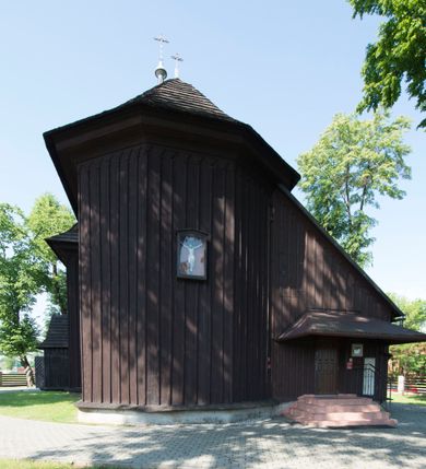 Zdjęcie nr 6: Kościół św. Jakuba w Palczowicach został wybudowany w roku 1894 w miejsce wcześniejszego kościoła z roku 1498. Kościół halowy, na kamiennej podmurówce, wzniesiony z drewna.  Kościół jest jednonawowy, orientowany.  Po jego zachodniej stronie szeroka, czworoboczna wieża nakryta ośmiobocznym hełmem. Pod hełmem również ośmioboczny szeroki, drewniany kandelabr. Hełm strzelisty, kryty gontem, zwieńczony metalowym krzyżem. Z czterech stron hełmu metalowe wykusze okienne  ze stylizowanymi sterczynami. Po czterech stronach korpusu wieży w jego wysokości małe otwory okienne  zwieńczone ostrokątnie. Korpus halowy nakryty dwuspadowym dachem z gontu.  We wschodniej części dachu ośmioboczna metalowa sygnaturka również zwieńczona krzyżem. Jej hełm strzelisty z pokryciem metalowym. W korpusie od południa i północy po dwa prostokątne otwory okienne z bliźniaczymi zamkniętymi ostrołukowo kwaterami. Prezbiterium niższe i węższe w stosunku do nawy, kryte osobnym, dwuspadowym dachem gontowym, zamknięte trójbocznie. Po południowej stronie prezbiterium dwa otwory okienne analogiczne do zlokalizowanych w nawie. Po północnej stronie prezbiterium dobudowana murowana, tynkowana zakrystia z dachem jednospadowym, krytym blachą.  W zakrystii jeden czworokątny otwór okienny i osobne wejście po stronie wschodniej. Nad głównym wejściem do kościoła, z czworobocznymi, dwuskrzydłowymi drzwiami  wysunięte dwuspadowe zadaszenie Po bokach drzwi w połowie ich wysokości symetrycznie ułożone, czworokątne otwory okienne. Do południowej ściany nawy głównej przylegająca drewniana kruchta na planie prostokątnym z dwuspadowym zadaszeniem zwieńczonym krzyżem. Po obu stronach drzwi otwory okienne zwieńczone ostrokątnie.