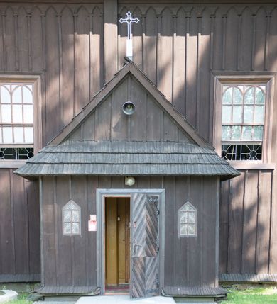 Zdjęcie nr 10: Kościół św. Jakuba w Palczowicach został wybudowany w roku 1894 w miejsce wcześniejszego kościoła z roku 1498. Kościół halowy, na kamiennej podmurówce, wzniesiony z drewna.  Kościół jest jednonawowy, orientowany.  Po jego zachodniej stronie szeroka, czworoboczna wieża nakryta ośmiobocznym hełmem. Pod hełmem również ośmioboczny szeroki, drewniany kandelabr. Hełm strzelisty, kryty gontem, zwieńczony metalowym krzyżem. Z czterech stron hełmu metalowe wykusze okienne  ze stylizowanymi sterczynami. Po czterech stronach korpusu wieży w jego wysokości małe otwory okienne  zwieńczone ostrokątnie. Korpus halowy nakryty dwuspadowym dachem z gontu.  We wschodniej części dachu ośmioboczna metalowa sygnaturka również zwieńczona krzyżem. Jej hełm strzelisty z pokryciem metalowym. W korpusie od południa i północy po dwa prostokątne otwory okienne z bliźniaczymi zamkniętymi ostrołukowo kwaterami. Prezbiterium niższe i węższe w stosunku do nawy, kryte osobnym, dwuspadowym dachem gontowym, zamknięte trójbocznie. Po południowej stronie prezbiterium dwa otwory okienne analogiczne do zlokalizowanych w nawie. Po północnej stronie prezbiterium dobudowana murowana, tynkowana zakrystia z dachem jednospadowym, krytym blachą.  W zakrystii jeden czworokątny otwór okienny i osobne wejście po stronie wschodniej. Nad głównym wejściem do kościoła, z czworobocznymi, dwuskrzydłowymi drzwiami  wysunięte dwuspadowe zadaszenie Po bokach drzwi w połowie ich wysokości symetrycznie ułożone, czworokątne otwory okienne. Do południowej ściany nawy głównej przylegająca drewniana kruchta na planie prostokątnym z dwuspadowym zadaszeniem zwieńczonym krzyżem. Po obu stronach drzwi otwory okienne zwieńczone ostrokątnie.