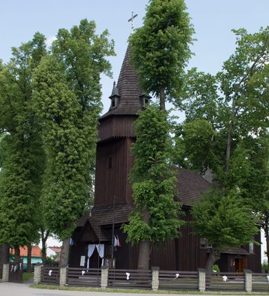 Zdjęcie nr 9: Kościół św. Jakuba w Palczowicach został wybudowany w roku 1894 w miejsce wcześniejszego kościoła z roku 1498. Kościół halowy, na kamiennej podmurówce, wzniesiony z drewna.  Kościół jest jednonawowy, orientowany.  Po jego zachodniej stronie szeroka, czworoboczna wieża nakryta ośmiobocznym hełmem. Pod hełmem również ośmioboczny szeroki, drewniany kandelabr. Hełm strzelisty, kryty gontem, zwieńczony metalowym krzyżem. Z czterech stron hełmu metalowe wykusze okienne  ze stylizowanymi sterczynami. Po czterech stronach korpusu wieży w jego wysokości małe otwory okienne  zwieńczone ostrokątnie. Korpus halowy nakryty dwuspadowym dachem z gontu.  We wschodniej części dachu ośmioboczna metalowa sygnaturka również zwieńczona krzyżem. Jej hełm strzelisty z pokryciem metalowym. W korpusie od południa i północy po dwa prostokątne otwory okienne z bliźniaczymi zamkniętymi ostrołukowo kwaterami. Prezbiterium niższe i węższe w stosunku do nawy, kryte osobnym, dwuspadowym dachem gontowym, zamknięte trójbocznie. Po południowej stronie prezbiterium dwa otwory okienne analogiczne do zlokalizowanych w nawie. Po północnej stronie prezbiterium dobudowana murowana, tynkowana zakrystia z dachem jednospadowym, krytym blachą.  W zakrystii jeden czworokątny otwór okienny i osobne wejście po stronie wschodniej. Nad głównym wejściem do kościoła, z czworobocznymi, dwuskrzydłowymi drzwiami  wysunięte dwuspadowe zadaszenie Po bokach drzwi w połowie ich wysokości symetrycznie ułożone, czworokątne otwory okienne. Do południowej ściany nawy głównej przylegająca drewniana kruchta na planie prostokątnym z dwuspadowym zadaszeniem zwieńczonym krzyżem. Po obu stronach drzwi otwory okienne zwieńczone ostrokątnie.