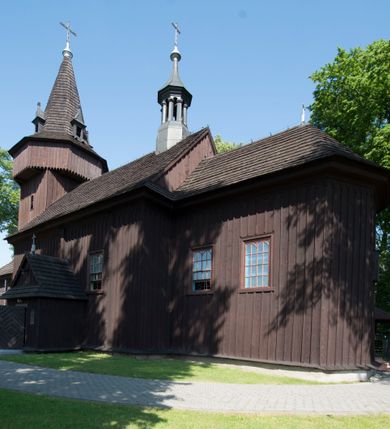 Zdjęcie nr 3: Kościół św. Jakuba w Palczowicach został wybudowany w roku 1894 w miejsce wcześniejszego kościoła z roku 1498. Kościół halowy, na kamiennej podmurówce, wzniesiony z drewna.  Kościół jest jednonawowy, orientowany.  Po jego zachodniej stronie szeroka, czworoboczna wieża nakryta ośmiobocznym hełmem. Pod hełmem również ośmioboczny szeroki, drewniany kandelabr. Hełm strzelisty, kryty gontem, zwieńczony metalowym krzyżem. Z czterech stron hełmu metalowe wykusze okienne  ze stylizowanymi sterczynami. Po czterech stronach korpusu wieży w jego wysokości małe otwory okienne  zwieńczone ostrokątnie. Korpus halowy nakryty dwuspadowym dachem z gontu.  We wschodniej części dachu ośmioboczna metalowa sygnaturka również zwieńczona krzyżem. Jej hełm strzelisty z pokryciem metalowym. W korpusie od południa i północy po dwa prostokątne otwory okienne z bliźniaczymi zamkniętymi ostrołukowo kwaterami. Prezbiterium niższe i węższe w stosunku do nawy, kryte osobnym, dwuspadowym dachem gontowym, zamknięte trójbocznie. Po południowej stronie prezbiterium dwa otwory okienne analogiczne do zlokalizowanych w nawie. Po północnej stronie prezbiterium dobudowana murowana, tynkowana zakrystia z dachem jednospadowym, krytym blachą.  W zakrystii jeden czworokątny otwór okienny i osobne wejście po stronie wschodniej. Nad głównym wejściem do kościoła, z czworobocznymi, dwuskrzydłowymi drzwiami  wysunięte dwuspadowe zadaszenie Po bokach drzwi w połowie ich wysokości symetrycznie ułożone, czworokątne otwory okienne. Do południowej ściany nawy głównej przylegająca drewniana kruchta na planie prostokątnym z dwuspadowym zadaszeniem zwieńczonym krzyżem. Po obu stronach drzwi otwory okienne zwieńczone ostrokątnie.
