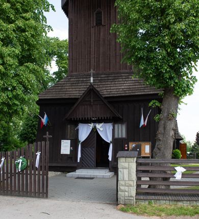 Zdjęcie nr 20: Kościół św. Jakuba w Palczowicach został wybudowany w roku 1894 w miejsce wcześniejszego kościoła z roku 1498. Kościół halowy, na kamiennej podmurówce, wzniesiony z drewna.  Kościół jest jednonawowy, orientowany.  Po jego zachodniej stronie szeroka, czworoboczna wieża nakryta ośmiobocznym hełmem. Pod hełmem również ośmioboczny szeroki, drewniany kandelabr. Hełm strzelisty, kryty gontem, zwieńczony metalowym krzyżem. Z czterech stron hełmu metalowe wykusze okienne  ze stylizowanymi sterczynami. Po czterech stronach korpusu wieży w jego wysokości małe otwory okienne  zwieńczone ostrokątnie. Korpus halowy nakryty dwuspadowym dachem z gontu.  We wschodniej części dachu ośmioboczna metalowa sygnaturka również zwieńczona krzyżem. Jej hełm strzelisty z pokryciem metalowym. W korpusie od południa i północy po dwa prostokątne otwory okienne z bliźniaczymi zamkniętymi ostrołukowo kwaterami. Prezbiterium niższe i węższe w stosunku do nawy, kryte osobnym, dwuspadowym dachem gontowym, zamknięte trójbocznie. Po południowej stronie prezbiterium dwa otwory okienne analogiczne do zlokalizowanych w nawie. Po północnej stronie prezbiterium dobudowana murowana, tynkowana zakrystia z dachem jednospadowym, krytym blachą.  W zakrystii jeden czworokątny otwór okienny i osobne wejście po stronie wschodniej. Nad głównym wejściem do kościoła, z czworobocznymi, dwuskrzydłowymi drzwiami  wysunięte dwuspadowe zadaszenie Po bokach drzwi w połowie ich wysokości symetrycznie ułożone, czworokątne otwory okienne. Do południowej ściany nawy głównej przylegająca drewniana kruchta na planie prostokątnym z dwuspadowym zadaszeniem zwieńczonym krzyżem. Po obu stronach drzwi otwory okienne zwieńczone ostrokątnie.