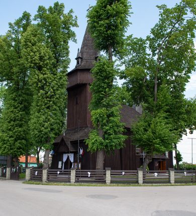 Zdjęcie nr 19: Kościół św. Jakuba w Palczowicach został wybudowany w roku 1894 w miejsce wcześniejszego kościoła z roku 1498. Kościół halowy, na kamiennej podmurówce, wzniesiony z drewna.  Kościół jest jednonawowy, orientowany.  Po jego zachodniej stronie szeroka, czworoboczna wieża nakryta ośmiobocznym hełmem. Pod hełmem również ośmioboczny szeroki, drewniany kandelabr. Hełm strzelisty, kryty gontem, zwieńczony metalowym krzyżem. Z czterech stron hełmu metalowe wykusze okienne  ze stylizowanymi sterczynami. Po czterech stronach korpusu wieży w jego wysokości małe otwory okienne  zwieńczone ostrokątnie. Korpus halowy nakryty dwuspadowym dachem z gontu.  We wschodniej części dachu ośmioboczna metalowa sygnaturka również zwieńczona krzyżem. Jej hełm strzelisty z pokryciem metalowym. W korpusie od południa i północy po dwa prostokątne otwory okienne z bliźniaczymi zamkniętymi ostrołukowo kwaterami. Prezbiterium niższe i węższe w stosunku do nawy, kryte osobnym, dwuspadowym dachem gontowym, zamknięte trójbocznie. Po południowej stronie prezbiterium dwa otwory okienne analogiczne do zlokalizowanych w nawie. Po północnej stronie prezbiterium dobudowana murowana, tynkowana zakrystia z dachem jednospadowym, krytym blachą.  W zakrystii jeden czworokątny otwór okienny i osobne wejście po stronie wschodniej. Nad głównym wejściem do kościoła, z czworobocznymi, dwuskrzydłowymi drzwiami  wysunięte dwuspadowe zadaszenie Po bokach drzwi w połowie ich wysokości symetrycznie ułożone, czworokątne otwory okienne. Do południowej ściany nawy głównej przylegająca drewniana kruchta na planie prostokątnym z dwuspadowym zadaszeniem zwieńczonym krzyżem. Po obu stronach drzwi otwory okienne zwieńczone ostrokątnie.