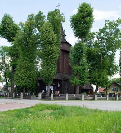 Zdjęcie nr 21: Kościół św. Jakuba w Palczowicach został wybudowany w roku 1894 w miejsce wcześniejszego kościoła z roku 1498. Kościół halowy, na kamiennej podmurówce, wzniesiony z drewna.  Kościół jest jednonawowy, orientowany.  Po jego zachodniej stronie szeroka, czworoboczna wieża nakryta ośmiobocznym hełmem. Pod hełmem również ośmioboczny szeroki, drewniany kandelabr. Hełm strzelisty, kryty gontem, zwieńczony metalowym krzyżem. Z czterech stron hełmu metalowe wykusze okienne  ze stylizowanymi sterczynami. Po czterech stronach korpusu wieży w jego wysokości małe otwory okienne  zwieńczone ostrokątnie. Korpus halowy nakryty dwuspadowym dachem z gontu.  We wschodniej części dachu ośmioboczna metalowa sygnaturka również zwieńczona krzyżem. Jej hełm strzelisty z pokryciem metalowym. W korpusie od południa i północy po dwa prostokątne otwory okienne z bliźniaczymi zamkniętymi ostrołukowo kwaterami. Prezbiterium niższe i węższe w stosunku do nawy, kryte osobnym, dwuspadowym dachem gontowym, zamknięte trójbocznie. Po południowej stronie prezbiterium dwa otwory okienne analogiczne do zlokalizowanych w nawie. Po północnej stronie prezbiterium dobudowana murowana, tynkowana zakrystia z dachem jednospadowym, krytym blachą.  W zakrystii jeden czworokątny otwór okienny i osobne wejście po stronie wschodniej. Nad głównym wejściem do kościoła, z czworobocznymi, dwuskrzydłowymi drzwiami  wysunięte dwuspadowe zadaszenie Po bokach drzwi w połowie ich wysokości symetrycznie ułożone, czworokątne otwory okienne. Do południowej ściany nawy głównej przylegająca drewniana kruchta na planie prostokątnym z dwuspadowym zadaszeniem zwieńczonym krzyżem. Po obu stronach drzwi otwory okienne zwieńczone ostrokątnie.