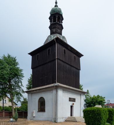 Zdjęcie nr 1: Dzwonnica na planie kwadratu do połowy wysokości murowana, wyżej drewniana, zwieńczona baniastym hełmem z latarnią. 
Część murowana nieco szersza. Od strony wschodniej znajdują się drzwi wejściowe, naroża są wzmocnione lizenami, od północy i południa znajdują się okna prostokątne zamknięte łukiem półokrągłym. Kondygnacje oddziela szeroki fartuch. Górna partia z pozorną izbicą przeprutą z każdej strony dwoma niewielkimi oknami w kształcie stojącego prostokąta zamkniętego łukiem pełnym. Od strony południowej otwór drzwiowy prostokątny zamknięty łukiem półokrągłym. Hełm baniasty przechodzi w oktogon,  na którym są arkadki wspierające mniejszy hełm cebulasty zwieńczony krzyżem. Dachy kryte blachą. 
