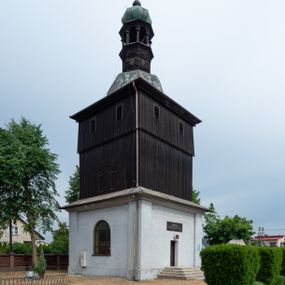 Zdjęcie nr 1: Dzwonnica na planie kwadratu do połowy wysokości murowana, wyżej drewniana, zwieńczona baniastym hełmem z latarnią. 
Część murowana nieco szersza. Od strony wschodniej znajdują się drzwi wejściowe, naroża są wzmocnione lizenami, od północy i południa znajdują się okna prostokątne zamknięte łukiem półokrągłym. Kondygnacje oddziela szeroki fartuch. Górna partia z pozorną izbicą przeprutą z każdej strony dwoma niewielkimi oknami w kształcie stojącego prostokąta zamkniętego łukiem pełnym. Od strony południowej otwór drzwiowy prostokątny zamknięty łukiem półokrągłym. Hełm baniasty przechodzi w oktogon,  na którym są arkadki wspierające mniejszy hełm cebulasty zwieńczony krzyżem. Dachy kryte blachą. 
