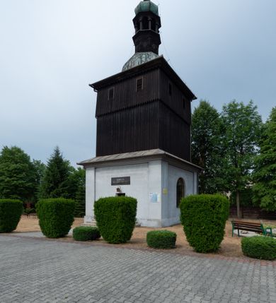 Zdjęcie nr 5: Dzwonnica na planie kwadratu do połowy wysokości murowana, wyżej drewniana, zwieńczona baniastym hełmem z latarnią. 
Część murowana nieco szersza. Od strony wschodniej znajdują się drzwi wejściowe, naroża są wzmocnione lizenami, od północy i południa znajdują się okna prostokątne zamknięte łukiem półokrągłym. Kondygnacje oddziela szeroki fartuch. Górna partia z pozorną izbicą przeprutą z każdej strony dwoma niewielkimi oknami w kształcie stojącego prostokąta zamkniętego łukiem pełnym. Od strony południowej otwór drzwiowy prostokątny zamknięty łukiem półokrągłym. Hełm baniasty przechodzi w oktogon,  na którym są arkadki wspierające mniejszy hełm cebulasty zwieńczony krzyżem. Dachy kryte blachą. 
