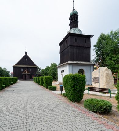 Zdjęcie nr 8: Dzwonnica na planie kwadratu do połowy wysokości murowana, wyżej drewniana, zwieńczona baniastym hełmem z latarnią. 
Część murowana nieco szersza. Od strony wschodniej znajdują się drzwi wejściowe, naroża są wzmocnione lizenami, od północy i południa znajdują się okna prostokątne zamknięte łukiem półokrągłym. Kondygnacje oddziela szeroki fartuch. Górna partia z pozorną izbicą przeprutą z każdej strony dwoma niewielkimi oknami w kształcie stojącego prostokąta zamkniętego łukiem pełnym. Od strony południowej otwór drzwiowy prostokątny zamknięty łukiem półokrągłym. Hełm baniasty przechodzi w oktogon,  na którym są arkadki wspierające mniejszy hełm cebulasty zwieńczony krzyżem. Dachy kryte blachą. 
