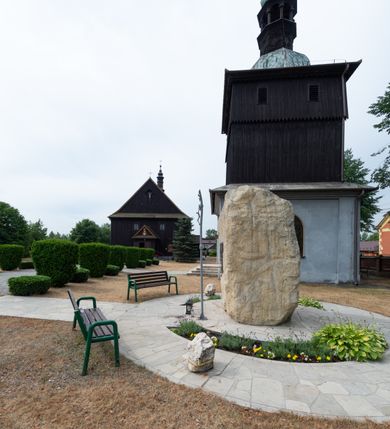 Zdjęcie nr 9: Dzwonnica na planie kwadratu do połowy wysokości murowana, wyżej drewniana, zwieńczona baniastym hełmem z latarnią. 
Część murowana nieco szersza. Od strony wschodniej znajdują się drzwi wejściowe, naroża są wzmocnione lizenami, od północy i południa znajdują się okna prostokątne zamknięte łukiem półokrągłym. Kondygnacje oddziela szeroki fartuch. Górna partia z pozorną izbicą przeprutą z każdej strony dwoma niewielkimi oknami w kształcie stojącego prostokąta zamkniętego łukiem pełnym. Od strony południowej otwór drzwiowy prostokątny zamknięty łukiem półokrągłym. Hełm baniasty przechodzi w oktogon,  na którym są arkadki wspierające mniejszy hełm cebulasty zwieńczony krzyżem. Dachy kryte blachą. 
