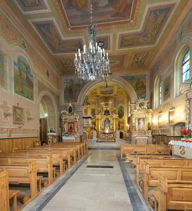 Zdjęcie nr 29: Kościół murowany, tynkowany, orientowany, jednonawowy. Prezbiterium prostokątne, krótkie, zamknięte trójbocznie, przy północnej ścianie prostokątna zakrystia z niższym przedsionkiem. Od wschodu, na zewnętrznej ścianie prezbiterium ogrójec. Nawa główna szersza od prezbiterium, na rzucie prostokąta, od północy przylega prostokątna kaplica, do której od zachodu dobudowany jest niski przedsionek, od południa przylega kruchta boczna, od zachodu prostokątny przedsionek z wieżą na planie kwadratu. Prezbiterium i nawa nakryte stropami, łuk tęczowy półkolisty, wewnątrz ujęty pilastrami, zakończony kluczem. Dostęp do kaplicy z nawy głównej przez wysokie przejście arkadowe na ścianie północnej, w południowej przejście do kruchty bocznej, na osi, pod chórem wejście do przedsionka. Kaplica boczna sklepiona kolebkowo. Fasada bez podziałów z wbudowaną wieżą, ujętą spłaszczonymi spływami. Na osi portal wejściowy flankowany dwoma pilastrami podtrzymującymi gzyms, na którym znajduje się półkoliste okno. W polu dwuskrzydłowe drzwi wejściowe ujęte opaską tynkową. Wieża dwukondygnacyjna, w dolnej kondygnacji okulus, w górnej okna w formie stojącego prostokąta zamkniętego łukiem półkolistym usytuowane z czterech stron. Na spływach ujmujących wieżę dwa okulusy. Wieża nakryta dachem ostrosłupowym. Południowa ściana oraz prezbiterium opięte grubymi szkarpami nakrytymi daszkami o nieregularnej wysokości. Do wschodniej ściany prezbiterium dobudowany murowany ogrojec flankowany filarami, nakryty wielospadowym daszkiem. Elewacje gładkie, tynkowane zakończone profilowanym gzymsem. Wejścia do kościoła przez przybudówkę kaplicy bocznej od północy oraz przez zachodni przedsionek i południową kruchtę. Okna w formie stojącego prostokąta zamkniętego łukiem półkolistym: siedem w elewacji południowej, trzy w północnej. Okna w formie stojącego prostokąta w dwóch kondygnacjach na północnej i południowej ścianie przedsionka zachodniego. Nawa główna, prezbiterium, kaplica i kruchta boczna nakryte dachem dwuspadowym, zakrystia i przybudówki dachami pulpitowymi. 
