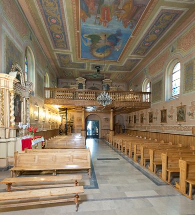 Zdjęcie nr 28: Kościół murowany, tynkowany, orientowany, jednonawowy. Prezbiterium prostokątne, krótkie, zamknięte trójbocznie, przy północnej ścianie prostokątna zakrystia z niższym przedsionkiem. Od wschodu, na zewnętrznej ścianie prezbiterium ogrójec. Nawa główna szersza od prezbiterium, na rzucie prostokąta, od północy przylega prostokątna kaplica, do której od zachodu dobudowany jest niski przedsionek, od południa przylega kruchta boczna, od zachodu prostokątny przedsionek z wieżą na planie kwadratu. Prezbiterium i nawa nakryte stropami, łuk tęczowy półkolisty, wewnątrz ujęty pilastrami, zakończony kluczem. Dostęp do kaplicy z nawy głównej przez wysokie przejście arkadowe na ścianie północnej, w południowej przejście do kruchty bocznej, na osi, pod chórem wejście do przedsionka. Kaplica boczna sklepiona kolebkowo. Fasada bez podziałów z wbudowaną wieżą, ujętą spłaszczonymi spływami. Na osi portal wejściowy flankowany dwoma pilastrami podtrzymującymi gzyms, na którym znajduje się półkoliste okno. W polu dwuskrzydłowe drzwi wejściowe ujęte opaską tynkową. Wieża dwukondygnacyjna, w dolnej kondygnacji okulus, w górnej okna w formie stojącego prostokąta zamkniętego łukiem półkolistym usytuowane z czterech stron. Na spływach ujmujących wieżę dwa okulusy. Wieża nakryta dachem ostrosłupowym. Południowa ściana oraz prezbiterium opięte grubymi szkarpami nakrytymi daszkami o nieregularnej wysokości. Do wschodniej ściany prezbiterium dobudowany murowany ogrojec flankowany filarami, nakryty wielospadowym daszkiem. Elewacje gładkie, tynkowane zakończone profilowanym gzymsem. Wejścia do kościoła przez przybudówkę kaplicy bocznej od północy oraz przez zachodni przedsionek i południową kruchtę. Okna w formie stojącego prostokąta zamkniętego łukiem półkolistym: siedem w elewacji południowej, trzy w północnej. Okna w formie stojącego prostokąta w dwóch kondygnacjach na północnej i południowej ścianie przedsionka zachodniego. Nawa główna, prezbiterium, kaplica i kruchta boczna nakryte dachem dwuspadowym, zakrystia i przybudówki dachami pulpitowymi. 
