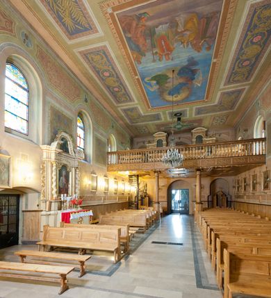 Zdjęcie nr 27: Kościół murowany, tynkowany, orientowany, jednonawowy. Prezbiterium prostokątne, krótkie, zamknięte trójbocznie, przy północnej ścianie prostokątna zakrystia z niższym przedsionkiem. Od wschodu, na zewnętrznej ścianie prezbiterium ogrójec. Nawa główna szersza od prezbiterium, na rzucie prostokąta, od północy przylega prostokątna kaplica, do której od zachodu dobudowany jest niski przedsionek, od południa przylega kruchta boczna, od zachodu prostokątny przedsionek z wieżą na planie kwadratu. Prezbiterium i nawa nakryte stropami, łuk tęczowy półkolisty, wewnątrz ujęty pilastrami, zakończony kluczem. Dostęp do kaplicy z nawy głównej przez wysokie przejście arkadowe na ścianie północnej, w południowej przejście do kruchty bocznej, na osi, pod chórem wejście do przedsionka. Kaplica boczna sklepiona kolebkowo. Fasada bez podziałów z wbudowaną wieżą, ujętą spłaszczonymi spływami. Na osi portal wejściowy flankowany dwoma pilastrami podtrzymującymi gzyms, na którym znajduje się półkoliste okno. W polu dwuskrzydłowe drzwi wejściowe ujęte opaską tynkową. Wieża dwukondygnacyjna, w dolnej kondygnacji okulus, w górnej okna w formie stojącego prostokąta zamkniętego łukiem półkolistym usytuowane z czterech stron. Na spływach ujmujących wieżę dwa okulusy. Wieża nakryta dachem ostrosłupowym. Południowa ściana oraz prezbiterium opięte grubymi szkarpami nakrytymi daszkami o nieregularnej wysokości. Do wschodniej ściany prezbiterium dobudowany murowany ogrojec flankowany filarami, nakryty wielospadowym daszkiem. Elewacje gładkie, tynkowane zakończone profilowanym gzymsem. Wejścia do kościoła przez przybudówkę kaplicy bocznej od północy oraz przez zachodni przedsionek i południową kruchtę. Okna w formie stojącego prostokąta zamkniętego łukiem półkolistym: siedem w elewacji południowej, trzy w północnej. Okna w formie stojącego prostokąta w dwóch kondygnacjach na północnej i południowej ścianie przedsionka zachodniego. Nawa główna, prezbiterium, kaplica i kruchta boczna nakryte dachem dwuspadowym, zakrystia i przybudówki dachami pulpitowymi. 
