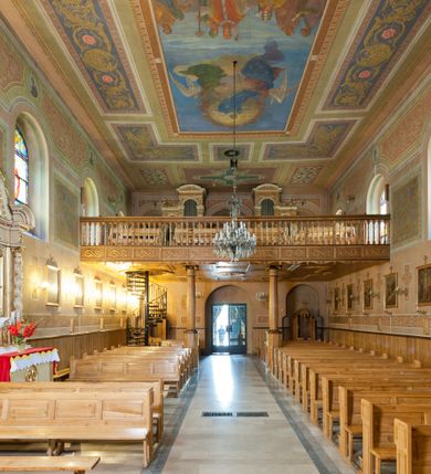 Zdjęcie nr 32: Kościół murowany, tynkowany, orientowany, jednonawowy. Prezbiterium prostokątne, krótkie, zamknięte trójbocznie, przy północnej ścianie prostokątna zakrystia z niższym przedsionkiem. Od wschodu, na zewnętrznej ścianie prezbiterium ogrójec. Nawa główna szersza od prezbiterium, na rzucie prostokąta, od północy przylega prostokątna kaplica, do której od zachodu dobudowany jest niski przedsionek, od południa przylega kruchta boczna, od zachodu prostokątny przedsionek z wieżą na planie kwadratu. Prezbiterium i nawa nakryte stropami, łuk tęczowy półkolisty, wewnątrz ujęty pilastrami, zakończony kluczem. Dostęp do kaplicy z nawy głównej przez wysokie przejście arkadowe na ścianie północnej, w południowej przejście do kruchty bocznej, na osi, pod chórem wejście do przedsionka. Kaplica boczna sklepiona kolebkowo. Fasada bez podziałów z wbudowaną wieżą, ujętą spłaszczonymi spływami. Na osi portal wejściowy flankowany dwoma pilastrami podtrzymującymi gzyms, na którym znajduje się półkoliste okno. W polu dwuskrzydłowe drzwi wejściowe ujęte opaską tynkową. Wieża dwukondygnacyjna, w dolnej kondygnacji okulus, w górnej okna w formie stojącego prostokąta zamkniętego łukiem półkolistym usytuowane z czterech stron. Na spływach ujmujących wieżę dwa okulusy. Wieża nakryta dachem ostrosłupowym. Południowa ściana oraz prezbiterium opięte grubymi szkarpami nakrytymi daszkami o nieregularnej wysokości. Do wschodniej ściany prezbiterium dobudowany murowany ogrojec flankowany filarami, nakryty wielospadowym daszkiem. Elewacje gładkie, tynkowane zakończone profilowanym gzymsem. Wejścia do kościoła przez przybudówkę kaplicy bocznej od północy oraz przez zachodni przedsionek i południową kruchtę. Okna w formie stojącego prostokąta zamkniętego łukiem półkolistym: siedem w elewacji południowej, trzy w północnej. Okna w formie stojącego prostokąta w dwóch kondygnacjach na północnej i południowej ścianie przedsionka zachodniego. Nawa główna, prezbiterium, kaplica i kruchta boczna nakryte dachem dwuspadowym, zakrystia i przybudówki dachami pulpitowymi. 
