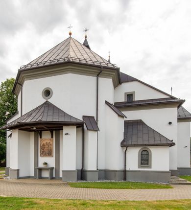 Zdjęcie nr 19: Kościół murowany, tynkowany, orientowany, jednonawowy. Prezbiterium prostokątne, krótkie, zamknięte trójbocznie, przy północnej ścianie prostokątna zakrystia z niższym przedsionkiem. Od wschodu, na zewnętrznej ścianie prezbiterium ogrójec. Nawa główna szersza od prezbiterium, na rzucie prostokąta, od północy przylega prostokątna kaplica, do której od zachodu dobudowany jest niski przedsionek, od południa przylega kruchta boczna, od zachodu prostokątny przedsionek z wieżą na planie kwadratu. Prezbiterium i nawa nakryte stropami, łuk tęczowy półkolisty, wewnątrz ujęty pilastrami, zakończony kluczem. Dostęp do kaplicy z nawy głównej przez wysokie przejście arkadowe na ścianie północnej, w południowej przejście do kruchty bocznej, na osi, pod chórem wejście do przedsionka. Kaplica boczna sklepiona kolebkowo. Fasada bez podziałów z wbudowaną wieżą, ujętą spłaszczonymi spływami. Na osi portal wejściowy flankowany dwoma pilastrami podtrzymującymi gzyms, na którym znajduje się półkoliste okno. W polu dwuskrzydłowe drzwi wejściowe ujęte opaską tynkową. Wieża dwukondygnacyjna, w dolnej kondygnacji okulus, w górnej okna w formie stojącego prostokąta zamkniętego łukiem półkolistym usytuowane z czterech stron. Na spływach ujmujących wieżę dwa okulusy. Wieża nakryta dachem ostrosłupowym. Południowa ściana oraz prezbiterium opięte grubymi szkarpami nakrytymi daszkami o nieregularnej wysokości. Do wschodniej ściany prezbiterium dobudowany murowany ogrojec flankowany filarami, nakryty wielospadowym daszkiem. Elewacje gładkie, tynkowane zakończone profilowanym gzymsem. Wejścia do kościoła przez przybudówkę kaplicy bocznej od północy oraz przez zachodni przedsionek i południową kruchtę. Okna w formie stojącego prostokąta zamkniętego łukiem półkolistym: siedem w elewacji południowej, trzy w północnej. Okna w formie stojącego prostokąta w dwóch kondygnacjach na północnej i południowej ścianie przedsionka zachodniego. Nawa główna, prezbiterium, kaplica i kruchta boczna nakryte dachem dwuspadowym, zakrystia i przybudówki dachami pulpitowymi. 
