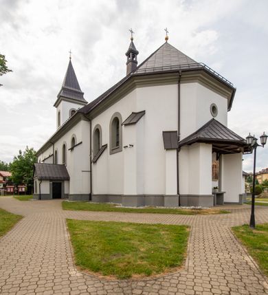 Zdjęcie nr 15: Kościół murowany, tynkowany, orientowany, jednonawowy. Prezbiterium prostokątne, krótkie, zamknięte trójbocznie, przy północnej ścianie prostokątna zakrystia z niższym przedsionkiem. Od wschodu, na zewnętrznej ścianie prezbiterium ogrójec. Nawa główna szersza od prezbiterium, na rzucie prostokąta, od północy przylega prostokątna kaplica, do której od zachodu dobudowany jest niski przedsionek, od południa przylega kruchta boczna, od zachodu prostokątny przedsionek z wieżą na planie kwadratu. Prezbiterium i nawa nakryte stropami, łuk tęczowy półkolisty, wewnątrz ujęty pilastrami, zakończony kluczem. Dostęp do kaplicy z nawy głównej przez wysokie przejście arkadowe na ścianie północnej, w południowej przejście do kruchty bocznej, na osi, pod chórem wejście do przedsionka. Kaplica boczna sklepiona kolebkowo. Fasada bez podziałów z wbudowaną wieżą, ujętą spłaszczonymi spływami. Na osi portal wejściowy flankowany dwoma pilastrami podtrzymującymi gzyms, na którym znajduje się półkoliste okno. W polu dwuskrzydłowe drzwi wejściowe ujęte opaską tynkową. Wieża dwukondygnacyjna, w dolnej kondygnacji okulus, w górnej okna w formie stojącego prostokąta zamkniętego łukiem półkolistym usytuowane z czterech stron. Na spływach ujmujących wieżę dwa okulusy. Wieża nakryta dachem ostrosłupowym. Południowa ściana oraz prezbiterium opięte grubymi szkarpami nakrytymi daszkami o nieregularnej wysokości. Do wschodniej ściany prezbiterium dobudowany murowany ogrojec flankowany filarami, nakryty wielospadowym daszkiem. Elewacje gładkie, tynkowane zakończone profilowanym gzymsem. Wejścia do kościoła przez przybudówkę kaplicy bocznej od północy oraz przez zachodni przedsionek i południową kruchtę. Okna w formie stojącego prostokąta zamkniętego łukiem półkolistym: siedem w elewacji południowej, trzy w północnej. Okna w formie stojącego prostokąta w dwóch kondygnacjach na północnej i południowej ścianie przedsionka zachodniego. Nawa główna, prezbiterium, kaplica i kruchta boczna nakryte dachem dwuspadowym, zakrystia i przybudówki dachami pulpitowymi. 
