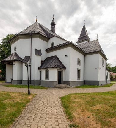 Zdjęcie nr 17: Kościół murowany, tynkowany, orientowany, jednonawowy. Prezbiterium prostokątne, krótkie, zamknięte trójbocznie, przy północnej ścianie prostokątna zakrystia z niższym przedsionkiem. Od wschodu, na zewnętrznej ścianie prezbiterium ogrójec. Nawa główna szersza od prezbiterium, na rzucie prostokąta, od północy przylega prostokątna kaplica, do której od zachodu dobudowany jest niski przedsionek, od południa przylega kruchta boczna, od zachodu prostokątny przedsionek z wieżą na planie kwadratu. Prezbiterium i nawa nakryte stropami, łuk tęczowy półkolisty, wewnątrz ujęty pilastrami, zakończony kluczem. Dostęp do kaplicy z nawy głównej przez wysokie przejście arkadowe na ścianie północnej, w południowej przejście do kruchty bocznej, na osi, pod chórem wejście do przedsionka. Kaplica boczna sklepiona kolebkowo. Fasada bez podziałów z wbudowaną wieżą, ujętą spłaszczonymi spływami. Na osi portal wejściowy flankowany dwoma pilastrami podtrzymującymi gzyms, na którym znajduje się półkoliste okno. W polu dwuskrzydłowe drzwi wejściowe ujęte opaską tynkową. Wieża dwukondygnacyjna, w dolnej kondygnacji okulus, w górnej okna w formie stojącego prostokąta zamkniętego łukiem półkolistym usytuowane z czterech stron. Na spływach ujmujących wieżę dwa okulusy. Wieża nakryta dachem ostrosłupowym. Południowa ściana oraz prezbiterium opięte grubymi szkarpami nakrytymi daszkami o nieregularnej wysokości. Do wschodniej ściany prezbiterium dobudowany murowany ogrojec flankowany filarami, nakryty wielospadowym daszkiem. Elewacje gładkie, tynkowane zakończone profilowanym gzymsem. Wejścia do kościoła przez przybudówkę kaplicy bocznej od północy oraz przez zachodni przedsionek i południową kruchtę. Okna w formie stojącego prostokąta zamkniętego łukiem półkolistym: siedem w elewacji południowej, trzy w północnej. Okna w formie stojącego prostokąta w dwóch kondygnacjach na północnej i południowej ścianie przedsionka zachodniego. Nawa główna, prezbiterium, kaplica i kruchta boczna nakryte dachem dwuspadowym, zakrystia i przybudówki dachami pulpitowymi. 
