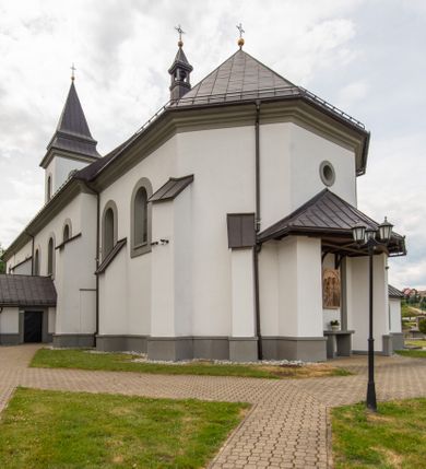 Zdjęcie nr 18: Kościół murowany, tynkowany, orientowany, jednonawowy. Prezbiterium prostokątne, krótkie, zamknięte trójbocznie, przy północnej ścianie prostokątna zakrystia z niższym przedsionkiem. Od wschodu, na zewnętrznej ścianie prezbiterium ogrójec. Nawa główna szersza od prezbiterium, na rzucie prostokąta, od północy przylega prostokątna kaplica, do której od zachodu dobudowany jest niski przedsionek, od południa przylega kruchta boczna, od zachodu prostokątny przedsionek z wieżą na planie kwadratu. Prezbiterium i nawa nakryte stropami, łuk tęczowy półkolisty, wewnątrz ujęty pilastrami, zakończony kluczem. Dostęp do kaplicy z nawy głównej przez wysokie przejście arkadowe na ścianie północnej, w południowej przejście do kruchty bocznej, na osi, pod chórem wejście do przedsionka. Kaplica boczna sklepiona kolebkowo. Fasada bez podziałów z wbudowaną wieżą, ujętą spłaszczonymi spływami. Na osi portal wejściowy flankowany dwoma pilastrami podtrzymującymi gzyms, na którym znajduje się półkoliste okno. W polu dwuskrzydłowe drzwi wejściowe ujęte opaską tynkową. Wieża dwukondygnacyjna, w dolnej kondygnacji okulus, w górnej okna w formie stojącego prostokąta zamkniętego łukiem półkolistym usytuowane z czterech stron. Na spływach ujmujących wieżę dwa okulusy. Wieża nakryta dachem ostrosłupowym. Południowa ściana oraz prezbiterium opięte grubymi szkarpami nakrytymi daszkami o nieregularnej wysokości. Do wschodniej ściany prezbiterium dobudowany murowany ogrojec flankowany filarami, nakryty wielospadowym daszkiem. Elewacje gładkie, tynkowane zakończone profilowanym gzymsem. Wejścia do kościoła przez przybudówkę kaplicy bocznej od północy oraz przez zachodni przedsionek i południową kruchtę. Okna w formie stojącego prostokąta zamkniętego łukiem półkolistym: siedem w elewacji południowej, trzy w północnej. Okna w formie stojącego prostokąta w dwóch kondygnacjach na północnej i południowej ścianie przedsionka zachodniego. Nawa główna, prezbiterium, kaplica i kruchta boczna nakryte dachem dwuspadowym, zakrystia i przybudówki dachami pulpitowymi. 
