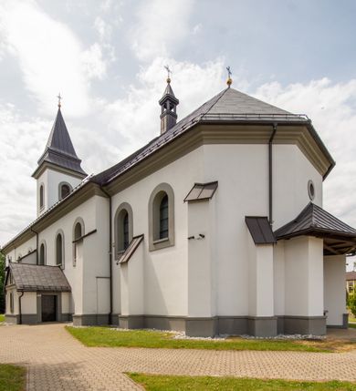 Zdjęcie nr 21: Kościół murowany, tynkowany, orientowany, jednonawowy. Prezbiterium prostokątne, krótkie, zamknięte trójbocznie, przy północnej ścianie prostokątna zakrystia z niższym przedsionkiem. Od wschodu, na zewnętrznej ścianie prezbiterium ogrójec. Nawa główna szersza od prezbiterium, na rzucie prostokąta, od północy przylega prostokątna kaplica, do której od zachodu dobudowany jest niski przedsionek, od południa przylega kruchta boczna, od zachodu prostokątny przedsionek z wieżą na planie kwadratu. Prezbiterium i nawa nakryte stropami, łuk tęczowy półkolisty, wewnątrz ujęty pilastrami, zakończony kluczem. Dostęp do kaplicy z nawy głównej przez wysokie przejście arkadowe na ścianie północnej, w południowej przejście do kruchty bocznej, na osi, pod chórem wejście do przedsionka. Kaplica boczna sklepiona kolebkowo. Fasada bez podziałów z wbudowaną wieżą, ujętą spłaszczonymi spływami. Na osi portal wejściowy flankowany dwoma pilastrami podtrzymującymi gzyms, na którym znajduje się półkoliste okno. W polu dwuskrzydłowe drzwi wejściowe ujęte opaską tynkową. Wieża dwukondygnacyjna, w dolnej kondygnacji okulus, w górnej okna w formie stojącego prostokąta zamkniętego łukiem półkolistym usytuowane z czterech stron. Na spływach ujmujących wieżę dwa okulusy. Wieża nakryta dachem ostrosłupowym. Południowa ściana oraz prezbiterium opięte grubymi szkarpami nakrytymi daszkami o nieregularnej wysokości. Do wschodniej ściany prezbiterium dobudowany murowany ogrojec flankowany filarami, nakryty wielospadowym daszkiem. Elewacje gładkie, tynkowane zakończone profilowanym gzymsem. Wejścia do kościoła przez przybudówkę kaplicy bocznej od północy oraz przez zachodni przedsionek i południową kruchtę. Okna w formie stojącego prostokąta zamkniętego łukiem półkolistym: siedem w elewacji południowej, trzy w północnej. Okna w formie stojącego prostokąta w dwóch kondygnacjach na północnej i południowej ścianie przedsionka zachodniego. Nawa główna, prezbiterium, kaplica i kruchta boczna nakryte dachem dwuspadowym, zakrystia i przybudówki dachami pulpitowymi. 
