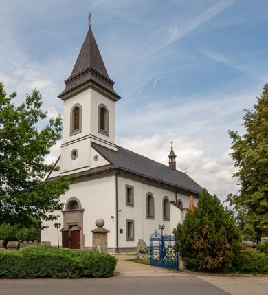 Zdjęcie nr 23: Kościół murowany, tynkowany, orientowany, jednonawowy. Prezbiterium prostokątne, krótkie, zamknięte trójbocznie, przy północnej ścianie prostokątna zakrystia z niższym przedsionkiem. Od wschodu, na zewnętrznej ścianie prezbiterium ogrójec. Nawa główna szersza od prezbiterium, na rzucie prostokąta, od północy przylega prostokątna kaplica, do której od zachodu dobudowany jest niski przedsionek, od południa przylega kruchta boczna, od zachodu prostokątny przedsionek z wieżą na planie kwadratu. Prezbiterium i nawa nakryte stropami, łuk tęczowy półkolisty, wewnątrz ujęty pilastrami, zakończony kluczem. Dostęp do kaplicy z nawy głównej przez wysokie przejście arkadowe na ścianie północnej, w południowej przejście do kruchty bocznej, na osi, pod chórem wejście do przedsionka. Kaplica boczna sklepiona kolebkowo. Fasada bez podziałów z wbudowaną wieżą, ujętą spłaszczonymi spływami. Na osi portal wejściowy flankowany dwoma pilastrami podtrzymującymi gzyms, na którym znajduje się półkoliste okno. W polu dwuskrzydłowe drzwi wejściowe ujęte opaską tynkową. Wieża dwukondygnacyjna, w dolnej kondygnacji okulus, w górnej okna w formie stojącego prostokąta zamkniętego łukiem półkolistym usytuowane z czterech stron. Na spływach ujmujących wieżę dwa okulusy. Wieża nakryta dachem ostrosłupowym. Południowa ściana oraz prezbiterium opięte grubymi szkarpami nakrytymi daszkami o nieregularnej wysokości. Do wschodniej ściany prezbiterium dobudowany murowany ogrojec flankowany filarami, nakryty wielospadowym daszkiem. Elewacje gładkie, tynkowane zakończone profilowanym gzymsem. Wejścia do kościoła przez przybudówkę kaplicy bocznej od północy oraz przez zachodni przedsionek i południową kruchtę. Okna w formie stojącego prostokąta zamkniętego łukiem półkolistym: siedem w elewacji południowej, trzy w północnej. Okna w formie stojącego prostokąta w dwóch kondygnacjach na północnej i południowej ścianie przedsionka zachodniego. Nawa główna, prezbiterium, kaplica i kruchta boczna nakryte dachem dwuspadowym, zakrystia i przybudówki dachami pulpitowymi. 

