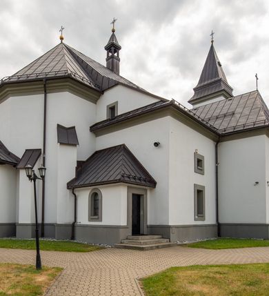 Zdjęcie nr 20: Kościół murowany, tynkowany, orientowany, jednonawowy. Prezbiterium prostokątne, krótkie, zamknięte trójbocznie, przy północnej ścianie prostokątna zakrystia z niższym przedsionkiem. Od wschodu, na zewnętrznej ścianie prezbiterium ogrójec. Nawa główna szersza od prezbiterium, na rzucie prostokąta, od północy przylega prostokątna kaplica, do której od zachodu dobudowany jest niski przedsionek, od południa przylega kruchta boczna, od zachodu prostokątny przedsionek z wieżą na planie kwadratu. Prezbiterium i nawa nakryte stropami, łuk tęczowy półkolisty, wewnątrz ujęty pilastrami, zakończony kluczem. Dostęp do kaplicy z nawy głównej przez wysokie przejście arkadowe na ścianie północnej, w południowej przejście do kruchty bocznej, na osi, pod chórem wejście do przedsionka. Kaplica boczna sklepiona kolebkowo. Fasada bez podziałów z wbudowaną wieżą, ujętą spłaszczonymi spływami. Na osi portal wejściowy flankowany dwoma pilastrami podtrzymującymi gzyms, na którym znajduje się półkoliste okno. W polu dwuskrzydłowe drzwi wejściowe ujęte opaską tynkową. Wieża dwukondygnacyjna, w dolnej kondygnacji okulus, w górnej okna w formie stojącego prostokąta zamkniętego łukiem półkolistym usytuowane z czterech stron. Na spływach ujmujących wieżę dwa okulusy. Wieża nakryta dachem ostrosłupowym. Południowa ściana oraz prezbiterium opięte grubymi szkarpami nakrytymi daszkami o nieregularnej wysokości. Do wschodniej ściany prezbiterium dobudowany murowany ogrojec flankowany filarami, nakryty wielospadowym daszkiem. Elewacje gładkie, tynkowane zakończone profilowanym gzymsem. Wejścia do kościoła przez przybudówkę kaplicy bocznej od północy oraz przez zachodni przedsionek i południową kruchtę. Okna w formie stojącego prostokąta zamkniętego łukiem półkolistym: siedem w elewacji południowej, trzy w północnej. Okna w formie stojącego prostokąta w dwóch kondygnacjach na północnej i południowej ścianie przedsionka zachodniego. Nawa główna, prezbiterium, kaplica i kruchta boczna nakryte dachem dwuspadowym, zakrystia i przybudówki dachami pulpitowymi. 
