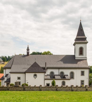 Zdjęcie nr 12: Kościół murowany, tynkowany, orientowany, jednonawowy. Prezbiterium prostokątne, krótkie, zamknięte trójbocznie, przy północnej ścianie prostokątna zakrystia z niższym przedsionkiem. Od wschodu, na zewnętrznej ścianie prezbiterium ogrójec. Nawa główna szersza od prezbiterium, na rzucie prostokąta, od północy przylega prostokątna kaplica, do której od zachodu dobudowany jest niski przedsionek, od południa przylega kruchta boczna, od zachodu prostokątny przedsionek z wieżą na planie kwadratu. Prezbiterium i nawa nakryte stropami, łuk tęczowy półkolisty, wewnątrz ujęty pilastrami, zakończony kluczem. Dostęp do kaplicy z nawy głównej przez wysokie przejście arkadowe na ścianie północnej, w południowej przejście do kruchty bocznej, na osi, pod chórem wejście do przedsionka. Kaplica boczna sklepiona kolebkowo. Fasada bez podziałów z wbudowaną wieżą, ujętą spłaszczonymi spływami. Na osi portal wejściowy flankowany dwoma pilastrami podtrzymującymi gzyms, na którym znajduje się półkoliste okno. W polu dwuskrzydłowe drzwi wejściowe ujęte opaską tynkową. Wieża dwukondygnacyjna, w dolnej kondygnacji okulus, w górnej okna w formie stojącego prostokąta zamkniętego łukiem półkolistym usytuowane z czterech stron. Na spływach ujmujących wieżę dwa okulusy. Wieża nakryta dachem ostrosłupowym. Południowa ściana oraz prezbiterium opięte grubymi szkarpami nakrytymi daszkami o nieregularnej wysokości. Do wschodniej ściany prezbiterium dobudowany murowany ogrojec flankowany filarami, nakryty wielospadowym daszkiem. Elewacje gładkie, tynkowane zakończone profilowanym gzymsem. Wejścia do kościoła przez przybudówkę kaplicy bocznej od północy oraz przez zachodni przedsionek i południową kruchtę. Okna w formie stojącego prostokąta zamkniętego łukiem półkolistym: siedem w elewacji południowej, trzy w północnej. Okna w formie stojącego prostokąta w dwóch kondygnacjach na północnej i południowej ścianie przedsionka zachodniego. Nawa główna, prezbiterium, kaplica i kruchta boczna nakryte dachem dwuspadowym, zakrystia i przybudówki dachami pulpitowymi. 
