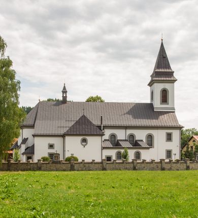 Zdjęcie nr 11: Kościół murowany, tynkowany, orientowany, jednonawowy. Prezbiterium prostokątne, krótkie, zamknięte trójbocznie, przy północnej ścianie prostokątna zakrystia z niższym przedsionkiem. Od wschodu, na zewnętrznej ścianie prezbiterium ogrójec. Nawa główna szersza od prezbiterium, na rzucie prostokąta, od północy przylega prostokątna kaplica, do której od zachodu dobudowany jest niski przedsionek, od południa przylega kruchta boczna, od zachodu prostokątny przedsionek z wieżą na planie kwadratu. Prezbiterium i nawa nakryte stropami, łuk tęczowy półkolisty, wewnątrz ujęty pilastrami, zakończony kluczem. Dostęp do kaplicy z nawy głównej przez wysokie przejście arkadowe na ścianie północnej, w południowej przejście do kruchty bocznej, na osi, pod chórem wejście do przedsionka. Kaplica boczna sklepiona kolebkowo. Fasada bez podziałów z wbudowaną wieżą, ujętą spłaszczonymi spływami. Na osi portal wejściowy flankowany dwoma pilastrami podtrzymującymi gzyms, na którym znajduje się półkoliste okno. W polu dwuskrzydłowe drzwi wejściowe ujęte opaską tynkową. Wieża dwukondygnacyjna, w dolnej kondygnacji okulus, w górnej okna w formie stojącego prostokąta zamkniętego łukiem półkolistym usytuowane z czterech stron. Na spływach ujmujących wieżę dwa okulusy. Wieża nakryta dachem ostrosłupowym. Południowa ściana oraz prezbiterium opięte grubymi szkarpami nakrytymi daszkami o nieregularnej wysokości. Do wschodniej ściany prezbiterium dobudowany murowany ogrojec flankowany filarami, nakryty wielospadowym daszkiem. Elewacje gładkie, tynkowane zakończone profilowanym gzymsem. Wejścia do kościoła przez przybudówkę kaplicy bocznej od północy oraz przez zachodni przedsionek i południową kruchtę. Okna w formie stojącego prostokąta zamkniętego łukiem półkolistym: siedem w elewacji południowej, trzy w północnej. Okna w formie stojącego prostokąta w dwóch kondygnacjach na północnej i południowej ścianie przedsionka zachodniego. Nawa główna, prezbiterium, kaplica i kruchta boczna nakryte dachem dwuspadowym, zakrystia i przybudówki dachami pulpitowymi. 
