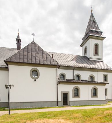 Zdjęcie nr 13: Kościół murowany, tynkowany, orientowany, jednonawowy. Prezbiterium prostokątne, krótkie, zamknięte trójbocznie, przy północnej ścianie prostokątna zakrystia z niższym przedsionkiem. Od wschodu, na zewnętrznej ścianie prezbiterium ogrójec. Nawa główna szersza od prezbiterium, na rzucie prostokąta, od północy przylega prostokątna kaplica, do której od zachodu dobudowany jest niski przedsionek, od południa przylega kruchta boczna, od zachodu prostokątny przedsionek z wieżą na planie kwadratu. Prezbiterium i nawa nakryte stropami, łuk tęczowy półkolisty, wewnątrz ujęty pilastrami, zakończony kluczem. Dostęp do kaplicy z nawy głównej przez wysokie przejście arkadowe na ścianie północnej, w południowej przejście do kruchty bocznej, na osi, pod chórem wejście do przedsionka. Kaplica boczna sklepiona kolebkowo. Fasada bez podziałów z wbudowaną wieżą, ujętą spłaszczonymi spływami. Na osi portal wejściowy flankowany dwoma pilastrami podtrzymującymi gzyms, na którym znajduje się półkoliste okno. W polu dwuskrzydłowe drzwi wejściowe ujęte opaską tynkową. Wieża dwukondygnacyjna, w dolnej kondygnacji okulus, w górnej okna w formie stojącego prostokąta zamkniętego łukiem półkolistym usytuowane z czterech stron. Na spływach ujmujących wieżę dwa okulusy. Wieża nakryta dachem ostrosłupowym. Południowa ściana oraz prezbiterium opięte grubymi szkarpami nakrytymi daszkami o nieregularnej wysokości. Do wschodniej ściany prezbiterium dobudowany murowany ogrojec flankowany filarami, nakryty wielospadowym daszkiem. Elewacje gładkie, tynkowane zakończone profilowanym gzymsem. Wejścia do kościoła przez przybudówkę kaplicy bocznej od północy oraz przez zachodni przedsionek i południową kruchtę. Okna w formie stojącego prostokąta zamkniętego łukiem półkolistym: siedem w elewacji południowej, trzy w północnej. Okna w formie stojącego prostokąta w dwóch kondygnacjach na północnej i południowej ścianie przedsionka zachodniego. Nawa główna, prezbiterium, kaplica i kruchta boczna nakryte dachem dwuspadowym, zakrystia i przybudówki dachami pulpitowymi. 
