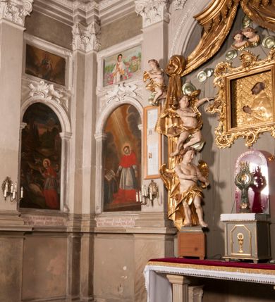 Zdjęcie nr 124: Kaplica zbudowana została na planie kwadratu i nakryta wzniesioną na pendentywach kopułą z latarnią. Przylega do kościoła od północy, do pierwszego przęsła nawy, z którą komunikuje się zamkniętym półkoliście przejściem. Wnętrze artykułowane jest w oparciu o schemat starożytnego łuku triumfalnego za pomocą osadzonych na wysokim cokole pilastrów z kompozytowymi głowicami. Pilastry podtrzymują wydatne belkowanie, ozodbione dekoracją stiukową w postaci puttów, festonów owocowych, rozet oraz kartuszy. Równocześnie pilastry ujmują półkoliste arkady, dwie niższe i większą, środkową. Niższe arkady wypełniają obrazy ze scenami z życia św. Karola Boromeusza. Ponad nimi w prostokątnych, stiukowych, obramieniach znajdują się malowane przedstawienia różnych świętych. W środkowej arkadzie ściany północnej umieszczono okazały późnobarokowy ołtarz z cudownym wizerunkiem św. Karola Boromeusza. Z kolei w arkadach wschodniej i zachodniej rozmieszczono prostokątne okna. Poniżej okna w arkadzie zachodniej znajduje się wyjście na zewnątrz kaplicy zaopatrzone w metalowe, prostokątne drzwi. Natomiast pod oknem w ścianie wschodniej zawieszono tablicę pamiątkową ku czci papieża Jana Pawła II. Arkadę wejściową do kaplicy zamyka prostokątna, brązowa krata. W jej podłuczu od wnętrza na wzór tympanonu umieszczono stiukowy kartusz z herbem Szreniawa, podtrzymywany przez dwa anioły. Ściany tarczowe podniebia przepruto czworobocznymi oknami ujętymi w stiukowe obramienia wolutowe. Na pendentywach przedstawiono w czterech stiukowych kartuszach herby: Szreniawa, Gryf i Kotwicz. Czwarty kartusz jest pusty. Czaszę kopuły wypełnia iluzjonistycznie malowana architektura podzielona na dwie strefy. Dolną artykułują pary pilastrów ujmujące okulusy oraz tralkowa balustrada, a górną gurty wyznaczające pola dla dekoracji ornamentalnej. Ściany zewnętrzne kaplicy zostały podzielone za pomocą kamiennych gzymsów i lizen na dwie trójosiowe kondygnacje, z których górna odpowiada wysokością smukłemu cokołowi mieszczącemu wejście. Zewnętrzne pola każdej elewacji dekorowane są płaskimi pasami tynku w układzie wzoru geometrycznego, zbliżonego do okuciowego. Okna i portal zostały ujęte w profilowane kamienne obramienia. Na ścianie północnej w środkowej kondygnacji pod kartuszem z herbem Szreniawa umieszczono tablicę fundacyjną z napisem: STANISLAUS COMES IN WIŚNICZ LUBOMIRSKI / PALATINUS ET GENERALIS CRACOVIEN[SIS] / SCEPUSIEN[SIS], BIALLOCERKIEVIEN[SIS] / ZATHORIEN[SIS], NIEPOLOMICIEN[SIS] E[T]C[ETER]A, E[T]C[ETER]A, CAPITANEUS / CAPELLAM HANC, / S[ANCTO] CAROLO BARRHOMAEO SUO TUTELARI PATRONO / POST RECEPTA SA[N]CTI HUIUS MERITIS TOT BENEFICIA / DICATAM / EX FUNDAMENTIS EREXIT, DONAVIT / EXORNAVIT, / ANNO D[O]MI[NI], 1640 (Stanisław hrabia na Wiśniczu Lubomirski wojewoda i starosta generalny krakowski, starosta spiski, białocerkiewski, zatorski, niepołomicki, i tak dalej, i tak dalej, tę kaplicę, poświęconą św. Karolowi Boromeuszowi, swojemu patronowi opiekuńczemu, po otrzymaniu tak wielkich łask za wstawiennictwem tego świetego, od fundamentów wzniósł, uposażył i ozdobił, roku Pańskiego 1640). Dach kaplicy oraz latarnia pokryte są blachą miedzianą.
