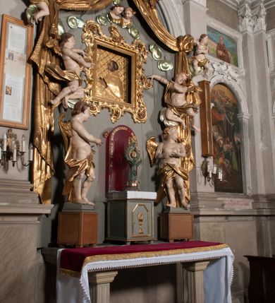 Zdjęcie nr 75: Kaplica zbudowana została na planie kwadratu i nakryta wzniesioną na pendentywach kopułą z latarnią. Przylega do kościoła od północy, do pierwszego przęsła nawy, z którą komunikuje się zamkniętym półkoliście przejściem. Wnętrze artykułowane jest w oparciu o schemat starożytnego łuku triumfalnego za pomocą osadzonych na wysokim cokole pilastrów z kompozytowymi głowicami. Pilastry podtrzymują wydatne belkowanie, ozodbione dekoracją stiukową w postaci puttów, festonów owocowych, rozet oraz kartuszy. Równocześnie pilastry ujmują półkoliste arkady, dwie niższe i większą, środkową. Niższe arkady wypełniają obrazy ze scenami z życia św. Karola Boromeusza. Ponad nimi w prostokątnych, stiukowych, obramieniach znajdują się malowane przedstawienia różnych świętych. W środkowej arkadzie ściany północnej umieszczono okazały późnobarokowy ołtarz z cudownym wizerunkiem św. Karola Boromeusza. Z kolei w arkadach wschodniej i zachodniej rozmieszczono prostokątne okna. Poniżej okna w arkadzie zachodniej znajduje się wyjście na zewnątrz kaplicy zaopatrzone w metalowe, prostokątne drzwi. Natomiast pod oknem w ścianie wschodniej zawieszono tablicę pamiątkową ku czci papieża Jana Pawła II. Arkadę wejściową do kaplicy zamyka prostokątna, brązowa krata. W jej podłuczu od wnętrza na wzór tympanonu umieszczono stiukowy kartusz z herbem Szreniawa, podtrzymywany przez dwa anioły. Ściany tarczowe podniebia przepruto czworobocznymi oknami ujętymi w stiukowe obramienia wolutowe. Na pendentywach przedstawiono w czterech stiukowych kartuszach herby: Szreniawa, Gryf i Kotwicz. Czwarty kartusz jest pusty. Czaszę kopuły wypełnia iluzjonistycznie malowana architektura podzielona na dwie strefy. Dolną artykułują pary pilastrów ujmujące okulusy oraz tralkowa balustrada, a górną gurty wyznaczające pola dla dekoracji ornamentalnej. Ściany zewnętrzne kaplicy zostały podzielone za pomocą kamiennych gzymsów i lizen na dwie trójosiowe kondygnacje, z których górna odpowiada wysokością smukłemu cokołowi mieszczącemu wejście. Zewnętrzne pola każdej elewacji dekorowane są płaskimi pasami tynku w układzie wzoru geometrycznego, zbliżonego do okuciowego. Okna i portal zostały ujęte w profilowane kamienne obramienia. Na ścianie północnej w środkowej kondygnacji pod kartuszem z herbem Szreniawa umieszczono tablicę fundacyjną z napisem: STANISLAUS COMES IN WIŚNICZ LUBOMIRSKI / PALATINUS ET GENERALIS CRACOVIEN[SIS] / SCEPUSIEN[SIS], BIALLOCERKIEVIEN[SIS] / ZATHORIEN[SIS], NIEPOLOMICIEN[SIS] E[T]C[ETER]A, E[T]C[ETER]A, CAPITANEUS / CAPELLAM HANC, / S[ANCTO] CAROLO BARRHOMAEO SUO TUTELARI PATRONO / POST RECEPTA SA[N]CTI HUIUS MERITIS TOT BENEFICIA / DICATAM / EX FUNDAMENTIS EREXIT, DONAVIT / EXORNAVIT, / ANNO D[O]MI[NI], 1640 (Stanisław hrabia na Wiśniczu Lubomirski wojewoda i starosta generalny krakowski, starosta spiski, białocerkiewski, zatorski, niepołomicki, i tak dalej, i tak dalej, tę kaplicę, poświęconą św. Karolowi Boromeuszowi, swojemu patronowi opiekuńczemu, po otrzymaniu tak wielkich łask za wstawiennictwem tego świetego, od fundamentów wzniósł, uposażył i ozdobił, roku Pańskiego 1640). Dach kaplicy oraz latarnia pokryte są blachą miedzianą.
