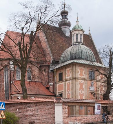 Zdjęcie nr 1: Kościół położony na południe od rynku, na placu otoczonym kamiennym murem z dwiema bramkami od zachodu i północy oraz bramką od południa. Kościół jednonawowy, dwuprzęsłowy, z węższym, niższym dwuprzęsłowym prezbiterium zamkniętym pięciobocznie. Do prezbiterium przylegają dwa aneksy, od północy dawna zakrystia (obecnie kaplica świętych Męczennic), zamknięta od wschodu dwubocznie, mająca w narożu z korpusem wieżyczkę schodową, a od południa zakrystia nowa, na planie prostokąta. Do nawy przylegają dwie kaplice: od północy kaplica Lubomirskich, założona na rzucie kwadratu, nakryta kopułą, a od południa kaplica Branickich, także na rzucie kwadratu z kopułą. Przy korpusie od zachodu piętrowa kruchta, pierwotnie otwarta w przyziemiu od północy, zachodu i południa ostrołukowymi arkadami. Arkada tęczy ostrołukowa. Sklepienie prezbiterium, zakrystii i obu kondygnacjach kruchty krzyżowo-żebrowe, w korpusie, pierwotnie trójprzęsłowym, pierwotnie sklepienie o polach trójkątnych z trójpromieniem, wsparte na dwóch dziesięciobocznych filarach, obecnie kolebkowo z lunetami. Żebra w prezbiterium i zakrystii o profilu żłobkowym, w kruchcie - gruszkowym. W prezbiterium służki cylindryczne, nadwieszone na oplecionych liśćmi wspornikach oraz rzeźbione zworniki z przedstawieniem Głowy Chrystusa i motywami roślinnymi. Ściany rozczłonkowane wykonanymi w czarnego marmuru arkadami, zamkniętymi łukiem półkolistymi. Okna ostrołukowe , obustronnie rozglifione z krzyżowym laskowaniem, w ścianie północnym prezbiterium ślepe. Kościół opięty przyporami. Elewacje na cokole, z profilowanymi gzymsami cokołowymi, kapnikowym i koronującym. Szczyty zwieńczone kwiatonami, z których zachodnie z krzyżem. Portale kamienne, ostrołukowe: zachodni profilowany, z ażurowym maswerkiem; drugi w prezbiterium do zakrystii, profilowany; trzeci do wieżyczki schodowej.