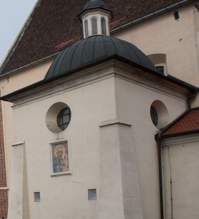 Zdjęcie nr 9: Kościół położony na południe od rynku, na placu otoczonym kamiennym murem z dwiema bramkami od zachodu i północy oraz bramką od południa. Kościół jednonawowy, dwuprzęsłowy, z węższym, niższym dwuprzęsłowym prezbiterium zamkniętym pięciobocznie. Do prezbiterium przylegają dwa aneksy, od północy dawna zakrystia (obecnie kaplica świętych Męczennic), zamknięta od wschodu dwubocznie, mająca w narożu z korpusem wieżyczkę schodową, a od południa zakrystia nowa, na planie prostokąta. Do nawy przylegają dwie kaplice: od północy kaplica Lubomirskich, założona na rzucie kwadratu, nakryta kopułą, a od południa kaplica Branickich, także na rzucie kwadratu z kopułą. Przy korpusie od zachodu piętrowa kruchta, pierwotnie otwarta w przyziemiu od północy, zachodu i południa ostrołukowymi arkadami. Arkada tęczy ostrołukowa. Sklepienie prezbiterium, zakrystii i obu kondygnacjach kruchty krzyżowo-żebrowe, w korpusie, pierwotnie trójprzęsłowym, pierwotnie sklepienie o polach trójkątnych z trójpromieniem, wsparte na dwóch dziesięciobocznych filarach, obecnie kolebkowo z lunetami. Żebra w prezbiterium i zakrystii o profilu żłobkowym, w kruchcie - gruszkowym. W prezbiterium służki cylindryczne, nadwieszone na oplecionych liśćmi wspornikach oraz rzeźbione zworniki z przedstawieniem Głowy Chrystusa i motywami roślinnymi. Ściany rozczłonkowane wykonanymi w czarnego marmuru arkadami, zamkniętymi łukiem półkolistymi. Okna ostrołukowe , obustronnie rozglifione z krzyżowym laskowaniem, w ścianie północnym prezbiterium ślepe. Kościół opięty przyporami. Elewacje na cokole, z profilowanymi gzymsami cokołowymi, kapnikowym i koronującym. Szczyty zwieńczone kwiatonami, z których zachodnie z krzyżem. Portale kamienne, ostrołukowe: zachodni profilowany, z ażurowym maswerkiem; drugi w prezbiterium do zakrystii, profilowany; trzeci do wieżyczki schodowej.