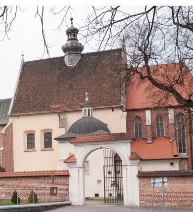 Zdjęcie nr 109: Kościół położony na południe od rynku, na placu otoczonym kamiennym murem z dwiema bramkami od zachodu i północy oraz bramką od południa. Kościół jednonawowy, dwuprzęsłowy, z węższym, niższym dwuprzęsłowym prezbiterium zamkniętym pięciobocznie. Do prezbiterium przylegają dwa aneksy, od północy dawna zakrystia (obecnie kaplica świętych Męczennic), zamknięta od wschodu dwubocznie, mająca w narożu z korpusem wieżyczkę schodową, a od południa zakrystia nowa, na planie prostokąta. Do nawy przylegają dwie kaplice: od północy kaplica Lubomirskich, założona na rzucie kwadratu, nakryta kopułą, a od południa kaplica Branickich, także na rzucie kwadratu z kopułą. Przy korpusie od zachodu piętrowa kruchta, pierwotnie otwarta w przyziemiu od północy, zachodu i południa ostrołukowymi arkadami. Arkada tęczy ostrołukowa. Sklepienie prezbiterium, zakrystii i obu kondygnacjach kruchty krzyżowo-żebrowe, w korpusie, pierwotnie trójprzęsłowym, pierwotnie sklepienie o polach trójkątnych z trójpromieniem, wsparte na dwóch dziesięciobocznych filarach, obecnie kolebkowo z lunetami. Żebra w prezbiterium i zakrystii o profilu żłobkowym, w kruchcie - gruszkowym. W prezbiterium służki cylindryczne, nadwieszone na oplecionych liśćmi wspornikach oraz rzeźbione zworniki z przedstawieniem Głowy Chrystusa i motywami roślinnymi. Ściany rozczłonkowane wykonanymi w czarnego marmuru arkadami, zamkniętymi łukiem półkolistymi. Okna ostrołukowe , obustronnie rozglifione z krzyżowym laskowaniem, w ścianie północnym prezbiterium ślepe. Kościół opięty przyporami. Elewacje na cokole, z profilowanymi gzymsami cokołowymi, kapnikowym i koronującym. Szczyty zwieńczone kwiatonami, z których zachodnie z krzyżem. Portale kamienne, ostrołukowe: zachodni profilowany, z ażurowym maswerkiem; drugi w prezbiterium do zakrystii, profilowany; trzeci do wieżyczki schodowej.