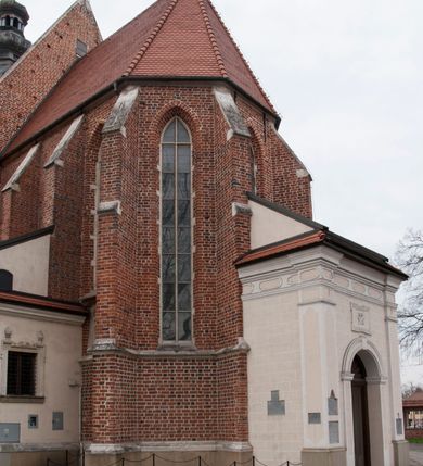 Zdjęcie nr 4: Kościół położony na południe od rynku, na placu otoczonym kamiennym murem z dwiema bramkami od zachodu i północy oraz bramką od południa. Kościół jednonawowy, dwuprzęsłowy, z węższym, niższym dwuprzęsłowym prezbiterium zamkniętym pięciobocznie. Do prezbiterium przylegają dwa aneksy, od północy dawna zakrystia (obecnie kaplica świętych Męczennic), zamknięta od wschodu dwubocznie, mająca w narożu z korpusem wieżyczkę schodową, a od południa zakrystia nowa, na planie prostokąta. Do nawy przylegają dwie kaplice: od północy kaplica Lubomirskich, założona na rzucie kwadratu, nakryta kopułą, a od południa kaplica Branickich, także na rzucie kwadratu z kopułą. Przy korpusie od zachodu piętrowa kruchta, pierwotnie otwarta w przyziemiu od północy, zachodu i południa ostrołukowymi arkadami. Arkada tęczy ostrołukowa. Sklepienie prezbiterium, zakrystii i obu kondygnacjach kruchty krzyżowo-żebrowe, w korpusie, pierwotnie trójprzęsłowym, pierwotnie sklepienie o polach trójkątnych z trójpromieniem, wsparte na dwóch dziesięciobocznych filarach, obecnie kolebkowo z lunetami. Żebra w prezbiterium i zakrystii o profilu żłobkowym, w kruchcie - gruszkowym. W prezbiterium służki cylindryczne, nadwieszone na oplecionych liśćmi wspornikach oraz rzeźbione zworniki z przedstawieniem Głowy Chrystusa i motywami roślinnymi. Ściany rozczłonkowane wykonanymi w czarnego marmuru arkadami, zamkniętymi łukiem półkolistymi. Okna ostrołukowe , obustronnie rozglifione z krzyżowym laskowaniem, w ścianie północnym prezbiterium ślepe. Kościół opięty przyporami. Elewacje na cokole, z profilowanymi gzymsami cokołowymi, kapnikowym i koronującym. Szczyty zwieńczone kwiatonami, z których zachodnie z krzyżem. Portale kamienne, ostrołukowe: zachodni profilowany, z ażurowym maswerkiem; drugi w prezbiterium do zakrystii, profilowany; trzeci do wieżyczki schodowej.
