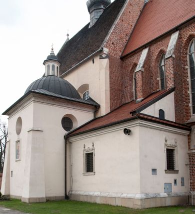 Zdjęcie nr 13: Kościół położony na południe od rynku, na placu otoczonym kamiennym murem z dwiema bramkami od zachodu i północy oraz bramką od południa. Kościół jednonawowy, dwuprzęsłowy, z węższym, niższym dwuprzęsłowym prezbiterium zamkniętym pięciobocznie. Do prezbiterium przylegają dwa aneksy, od północy dawna zakrystia (obecnie kaplica świętych Męczennic), zamknięta od wschodu dwubocznie, mająca w narożu z korpusem wieżyczkę schodową, a od południa zakrystia nowa, na planie prostokąta. Do nawy przylegają dwie kaplice: od północy kaplica Lubomirskich, założona na rzucie kwadratu, nakryta kopułą, a od południa kaplica Branickich, także na rzucie kwadratu z kopułą. Przy korpusie od zachodu piętrowa kruchta, pierwotnie otwarta w przyziemiu od północy, zachodu i południa ostrołukowymi arkadami. Arkada tęczy ostrołukowa. Sklepienie prezbiterium, zakrystii i obu kondygnacjach kruchty krzyżowo-żebrowe, w korpusie, pierwotnie trójprzęsłowym, pierwotnie sklepienie o polach trójkątnych z trójpromieniem, wsparte na dwóch dziesięciobocznych filarach, obecnie kolebkowo z lunetami. Żebra w prezbiterium i zakrystii o profilu żłobkowym, w kruchcie - gruszkowym. W prezbiterium służki cylindryczne, nadwieszone na oplecionych liśćmi wspornikach oraz rzeźbione zworniki z przedstawieniem Głowy Chrystusa i motywami roślinnymi. Ściany rozczłonkowane wykonanymi w czarnego marmuru arkadami, zamkniętymi łukiem półkolistymi. Okna ostrołukowe , obustronnie rozglifione z krzyżowym laskowaniem, w ścianie północnym prezbiterium ślepe. Kościół opięty przyporami. Elewacje na cokole, z profilowanymi gzymsami cokołowymi, kapnikowym i koronującym. Szczyty zwieńczone kwiatonami, z których zachodnie z krzyżem. Portale kamienne, ostrołukowe: zachodni profilowany, z ażurowym maswerkiem; drugi w prezbiterium do zakrystii, profilowany; trzeci do wieżyczki schodowej.