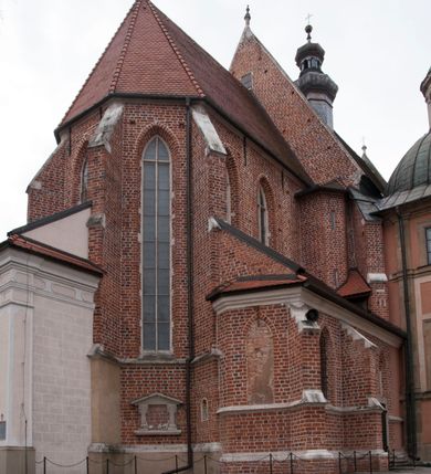 Zdjęcie nr 14: Kościół położony na południe od rynku, na placu otoczonym kamiennym murem z dwiema bramkami od zachodu i północy oraz bramką od południa. Kościół jednonawowy, dwuprzęsłowy, z węższym, niższym dwuprzęsłowym prezbiterium zamkniętym pięciobocznie. Do prezbiterium przylegają dwa aneksy, od północy dawna zakrystia (obecnie kaplica świętych Męczennic), zamknięta od wschodu dwubocznie, mająca w narożu z korpusem wieżyczkę schodową, a od południa zakrystia nowa, na planie prostokąta. Do nawy przylegają dwie kaplice: od północy kaplica Lubomirskich, założona na rzucie kwadratu, nakryta kopułą, a od południa kaplica Branickich, także na rzucie kwadratu z kopułą. Przy korpusie od zachodu piętrowa kruchta, pierwotnie otwarta w przyziemiu od północy, zachodu i południa ostrołukowymi arkadami. Arkada tęczy ostrołukowa. Sklepienie prezbiterium, zakrystii i obu kondygnacjach kruchty krzyżowo-żebrowe, w korpusie, pierwotnie trójprzęsłowym, pierwotnie sklepienie o polach trójkątnych z trójpromieniem, wsparte na dwóch dziesięciobocznych filarach, obecnie kolebkowo z lunetami. Żebra w prezbiterium i zakrystii o profilu żłobkowym, w kruchcie - gruszkowym. W prezbiterium służki cylindryczne, nadwieszone na oplecionych liśćmi wspornikach oraz rzeźbione zworniki z przedstawieniem Głowy Chrystusa i motywami roślinnymi. Ściany rozczłonkowane wykonanymi w czarnego marmuru arkadami, zamkniętymi łukiem półkolistymi. Okna ostrołukowe , obustronnie rozglifione z krzyżowym laskowaniem, w ścianie północnym prezbiterium ślepe. Kościół opięty przyporami. Elewacje na cokole, z profilowanymi gzymsami cokołowymi, kapnikowym i koronującym. Szczyty zwieńczone kwiatonami, z których zachodnie z krzyżem. Portale kamienne, ostrołukowe: zachodni profilowany, z ażurowym maswerkiem; drugi w prezbiterium do zakrystii, profilowany; trzeci do wieżyczki schodowej.