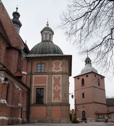 Zdjęcie nr 110: Kościół położony na południe od rynku, na placu otoczonym kamiennym murem z dwiema bramkami od zachodu i północy oraz bramką od południa. Kościół jednonawowy, dwuprzęsłowy, z węższym, niższym dwuprzęsłowym prezbiterium zamkniętym pięciobocznie. Do prezbiterium przylegają dwa aneksy, od północy dawna zakrystia (obecnie kaplica świętych Męczennic), zamknięta od wschodu dwubocznie, mająca w narożu z korpusem wieżyczkę schodową, a od południa zakrystia nowa, na planie prostokąta. Do nawy przylegają dwie kaplice: od północy kaplica Lubomirskich, założona na rzucie kwadratu, nakryta kopułą, a od południa kaplica Branickich, także na rzucie kwadratu z kopułą. Przy korpusie od zachodu piętrowa kruchta, pierwotnie otwarta w przyziemiu od północy, zachodu i południa ostrołukowymi arkadami. Arkada tęczy ostrołukowa. Sklepienie prezbiterium, zakrystii i obu kondygnacjach kruchty krzyżowo-żebrowe, w korpusie, pierwotnie trójprzęsłowym, pierwotnie sklepienie o polach trójkątnych z trójpromieniem, wsparte na dwóch dziesięciobocznych filarach, obecnie kolebkowo z lunetami. Żebra w prezbiterium i zakrystii o profilu żłobkowym, w kruchcie - gruszkowym. W prezbiterium służki cylindryczne, nadwieszone na oplecionych liśćmi wspornikach oraz rzeźbione zworniki z przedstawieniem Głowy Chrystusa i motywami roślinnymi. Ściany rozczłonkowane wykonanymi w czarnego marmuru arkadami, zamkniętymi łukiem półkolistymi. Okna ostrołukowe , obustronnie rozglifione z krzyżowym laskowaniem, w ścianie północnym prezbiterium ślepe. Kościół opięty przyporami. Elewacje na cokole, z profilowanymi gzymsami cokołowymi, kapnikowym i koronującym. Szczyty zwieńczone kwiatonami, z których zachodnie z krzyżem. Portale kamienne, ostrołukowe: zachodni profilowany, z ażurowym maswerkiem; drugi w prezbiterium do zakrystii, profilowany; trzeci do wieżyczki schodowej.