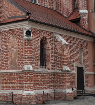 Zdjęcie nr 111: Kościół położony na południe od rynku, na placu otoczonym kamiennym murem z dwiema bramkami od zachodu i północy oraz bramką od południa. Kościół jednonawowy, dwuprzęsłowy, z węższym, niższym dwuprzęsłowym prezbiterium zamkniętym pięciobocznie. Do prezbiterium przylegają dwa aneksy, od północy dawna zakrystia (obecnie kaplica świętych Męczennic), zamknięta od wschodu dwubocznie, mająca w narożu z korpusem wieżyczkę schodową, a od południa zakrystia nowa, na planie prostokąta. Do nawy przylegają dwie kaplice: od północy kaplica Lubomirskich, założona na rzucie kwadratu, nakryta kopułą, a od południa kaplica Branickich, także na rzucie kwadratu z kopułą. Przy korpusie od zachodu piętrowa kruchta, pierwotnie otwarta w przyziemiu od północy, zachodu i południa ostrołukowymi arkadami. Arkada tęczy ostrołukowa. Sklepienie prezbiterium, zakrystii i obu kondygnacjach kruchty krzyżowo-żebrowe, w korpusie, pierwotnie trójprzęsłowym, pierwotnie sklepienie o polach trójkątnych z trójpromieniem, wsparte na dwóch dziesięciobocznych filarach, obecnie kolebkowo z lunetami. Żebra w prezbiterium i zakrystii o profilu żłobkowym, w kruchcie - gruszkowym. W prezbiterium służki cylindryczne, nadwieszone na oplecionych liśćmi wspornikach oraz rzeźbione zworniki z przedstawieniem Głowy Chrystusa i motywami roślinnymi. Ściany rozczłonkowane wykonanymi w czarnego marmuru arkadami, zamkniętymi łukiem półkolistymi. Okna ostrołukowe , obustronnie rozglifione z krzyżowym laskowaniem, w ścianie północnym prezbiterium ślepe. Kościół opięty przyporami. Elewacje na cokole, z profilowanymi gzymsami cokołowymi, kapnikowym i koronującym. Szczyty zwieńczone kwiatonami, z których zachodnie z krzyżem. Portale kamienne, ostrołukowe: zachodni profilowany, z ażurowym maswerkiem; drugi w prezbiterium do zakrystii, profilowany; trzeci do wieżyczki schodowej.