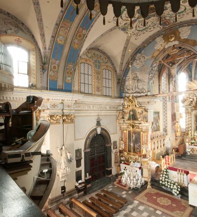 Zdjęcie nr 29: Kościół położony na południe od rynku, na placu otoczonym kamiennym murem z dwiema bramkami od zachodu i północy oraz bramką od południa. Kościół jednonawowy, dwuprzęsłowy, z węższym, niższym dwuprzęsłowym prezbiterium zamkniętym pięciobocznie. Do prezbiterium przylegają dwa aneksy, od północy dawna zakrystia (obecnie kaplica świętych Męczennic), zamknięta od wschodu dwubocznie, mająca w narożu z korpusem wieżyczkę schodową, a od południa zakrystia nowa, na planie prostokąta. Do nawy przylegają dwie kaplice: od północy kaplica Lubomirskich, założona na rzucie kwadratu, nakryta kopułą, a od południa kaplica Branickich, także na rzucie kwadratu z kopułą. Przy korpusie od zachodu piętrowa kruchta, pierwotnie otwarta w przyziemiu od północy, zachodu i południa ostrołukowymi arkadami. Arkada tęczy ostrołukowa. Sklepienie prezbiterium, zakrystii i obu kondygnacjach kruchty krzyżowo-żebrowe, w korpusie, pierwotnie trójprzęsłowym, pierwotnie sklepienie o polach trójkątnych z trójpromieniem, wsparte na dwóch dziesięciobocznych filarach, obecnie kolebkowo z lunetami. Żebra w prezbiterium i zakrystii o profilu żłobkowym, w kruchcie - gruszkowym. W prezbiterium służki cylindryczne, nadwieszone na oplecionych liśćmi wspornikach oraz rzeźbione zworniki z przedstawieniem Głowy Chrystusa i motywami roślinnymi. Ściany rozczłonkowane wykonanymi w czarnego marmuru arkadami, zamkniętymi łukiem półkolistymi. Okna ostrołukowe , obustronnie rozglifione z krzyżowym laskowaniem, w ścianie północnym prezbiterium ślepe. Kościół opięty przyporami. Elewacje na cokole, z profilowanymi gzymsami cokołowymi, kapnikowym i koronującym. Szczyty zwieńczone kwiatonami, z których zachodnie z krzyżem. Portale kamienne, ostrołukowe: zachodni profilowany, z ażurowym maswerkiem; drugi w prezbiterium do zakrystii, profilowany; trzeci do wieżyczki schodowej.