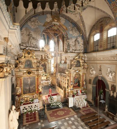 Zdjęcie nr 31: Kościół położony na południe od rynku, na placu otoczonym kamiennym murem z dwiema bramkami od zachodu i północy oraz bramką od południa. Kościół jednonawowy, dwuprzęsłowy, z węższym, niższym dwuprzęsłowym prezbiterium zamkniętym pięciobocznie. Do prezbiterium przylegają dwa aneksy, od północy dawna zakrystia (obecnie kaplica świętych Męczennic), zamknięta od wschodu dwubocznie, mająca w narożu z korpusem wieżyczkę schodową, a od południa zakrystia nowa, na planie prostokąta. Do nawy przylegają dwie kaplice: od północy kaplica Lubomirskich, założona na rzucie kwadratu, nakryta kopułą, a od południa kaplica Branickich, także na rzucie kwadratu z kopułą. Przy korpusie od zachodu piętrowa kruchta, pierwotnie otwarta w przyziemiu od północy, zachodu i południa ostrołukowymi arkadami. Arkada tęczy ostrołukowa. Sklepienie prezbiterium, zakrystii i obu kondygnacjach kruchty krzyżowo-żebrowe, w korpusie, pierwotnie trójprzęsłowym, pierwotnie sklepienie o polach trójkątnych z trójpromieniem, wsparte na dwóch dziesięciobocznych filarach, obecnie kolebkowo z lunetami. Żebra w prezbiterium i zakrystii o profilu żłobkowym, w kruchcie - gruszkowym. W prezbiterium służki cylindryczne, nadwieszone na oplecionych liśćmi wspornikach oraz rzeźbione zworniki z przedstawieniem Głowy Chrystusa i motywami roślinnymi. Ściany rozczłonkowane wykonanymi w czarnego marmuru arkadami, zamkniętymi łukiem półkolistymi. Okna ostrołukowe , obustronnie rozglifione z krzyżowym laskowaniem, w ścianie północnym prezbiterium ślepe. Kościół opięty przyporami. Elewacje na cokole, z profilowanymi gzymsami cokołowymi, kapnikowym i koronującym. Szczyty zwieńczone kwiatonami, z których zachodnie z krzyżem. Portale kamienne, ostrołukowe: zachodni profilowany, z ażurowym maswerkiem; drugi w prezbiterium do zakrystii, profilowany; trzeci do wieżyczki schodowej.