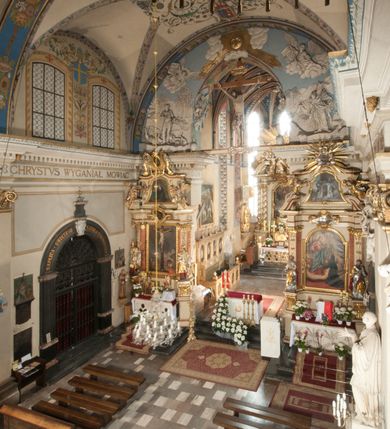 Zdjęcie nr 28: Kościół położony na południe od rynku, na placu otoczonym kamiennym murem z dwiema bramkami od zachodu i północy oraz bramką od południa. Kościół jednonawowy, dwuprzęsłowy, z węższym, niższym dwuprzęsłowym prezbiterium zamkniętym pięciobocznie. Do prezbiterium przylegają dwa aneksy, od północy dawna zakrystia (obecnie kaplica świętych Męczennic), zamknięta od wschodu dwubocznie, mająca w narożu z korpusem wieżyczkę schodową, a od południa zakrystia nowa, na planie prostokąta. Do nawy przylegają dwie kaplice: od północy kaplica Lubomirskich, założona na rzucie kwadratu, nakryta kopułą, a od południa kaplica Branickich, także na rzucie kwadratu z kopułą. Przy korpusie od zachodu piętrowa kruchta, pierwotnie otwarta w przyziemiu od północy, zachodu i południa ostrołukowymi arkadami. Arkada tęczy ostrołukowa. Sklepienie prezbiterium, zakrystii i obu kondygnacjach kruchty krzyżowo-żebrowe, w korpusie, pierwotnie trójprzęsłowym, pierwotnie sklepienie o polach trójkątnych z trójpromieniem, wsparte na dwóch dziesięciobocznych filarach, obecnie kolebkowo z lunetami. Żebra w prezbiterium i zakrystii o profilu żłobkowym, w kruchcie - gruszkowym. W prezbiterium służki cylindryczne, nadwieszone na oplecionych liśćmi wspornikach oraz rzeźbione zworniki z przedstawieniem Głowy Chrystusa i motywami roślinnymi. Ściany rozczłonkowane wykonanymi w czarnego marmuru arkadami, zamkniętymi łukiem półkolistymi. Okna ostrołukowe , obustronnie rozglifione z krzyżowym laskowaniem, w ścianie północnym prezbiterium ślepe. Kościół opięty przyporami. Elewacje na cokole, z profilowanymi gzymsami cokołowymi, kapnikowym i koronującym. Szczyty zwieńczone kwiatonami, z których zachodnie z krzyżem. Portale kamienne, ostrołukowe: zachodni profilowany, z ażurowym maswerkiem; drugi w prezbiterium do zakrystii, profilowany; trzeci do wieżyczki schodowej.