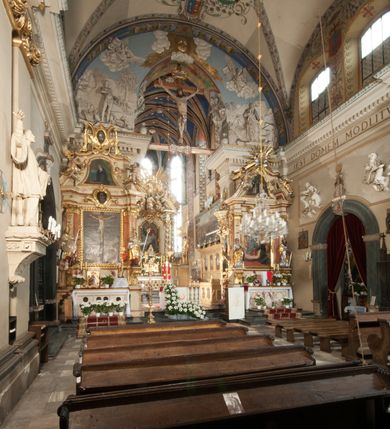 Zdjęcie nr 32: Kościół położony na południe od rynku, na placu otoczonym kamiennym murem z dwiema bramkami od zachodu i północy oraz bramką od południa. Kościół jednonawowy, dwuprzęsłowy, z węższym, niższym dwuprzęsłowym prezbiterium zamkniętym pięciobocznie. Do prezbiterium przylegają dwa aneksy, od północy dawna zakrystia (obecnie kaplica świętych Męczennic), zamknięta od wschodu dwubocznie, mająca w narożu z korpusem wieżyczkę schodową, a od południa zakrystia nowa, na planie prostokąta. Do nawy przylegają dwie kaplice: od północy kaplica Lubomirskich, założona na rzucie kwadratu, nakryta kopułą, a od południa kaplica Branickich, także na rzucie kwadratu z kopułą. Przy korpusie od zachodu piętrowa kruchta, pierwotnie otwarta w przyziemiu od północy, zachodu i południa ostrołukowymi arkadami. Arkada tęczy ostrołukowa. Sklepienie prezbiterium, zakrystii i obu kondygnacjach kruchty krzyżowo-żebrowe, w korpusie, pierwotnie trójprzęsłowym, pierwotnie sklepienie o polach trójkątnych z trójpromieniem, wsparte na dwóch dziesięciobocznych filarach, obecnie kolebkowo z lunetami. Żebra w prezbiterium i zakrystii o profilu żłobkowym, w kruchcie - gruszkowym. W prezbiterium służki cylindryczne, nadwieszone na oplecionych liśćmi wspornikach oraz rzeźbione zworniki z przedstawieniem Głowy Chrystusa i motywami roślinnymi. Ściany rozczłonkowane wykonanymi w czarnego marmuru arkadami, zamkniętymi łukiem półkolistymi. Okna ostrołukowe , obustronnie rozglifione z krzyżowym laskowaniem, w ścianie północnym prezbiterium ślepe. Kościół opięty przyporami. Elewacje na cokole, z profilowanymi gzymsami cokołowymi, kapnikowym i koronującym. Szczyty zwieńczone kwiatonami, z których zachodnie z krzyżem. Portale kamienne, ostrołukowe: zachodni profilowany, z ażurowym maswerkiem; drugi w prezbiterium do zakrystii, profilowany; trzeci do wieżyczki schodowej.