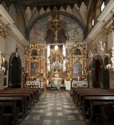 Zdjęcie nr 35: Kościół położony na południe od rynku, na placu otoczonym kamiennym murem z dwiema bramkami od zachodu i północy oraz bramką od południa. Kościół jednonawowy, dwuprzęsłowy, z węższym, niższym dwuprzęsłowym prezbiterium zamkniętym pięciobocznie. Do prezbiterium przylegają dwa aneksy, od północy dawna zakrystia (obecnie kaplica świętych Męczennic), zamknięta od wschodu dwubocznie, mająca w narożu z korpusem wieżyczkę schodową, a od południa zakrystia nowa, na planie prostokąta. Do nawy przylegają dwie kaplice: od północy kaplica Lubomirskich, założona na rzucie kwadratu, nakryta kopułą, a od południa kaplica Branickich, także na rzucie kwadratu z kopułą. Przy korpusie od zachodu piętrowa kruchta, pierwotnie otwarta w przyziemiu od północy, zachodu i południa ostrołukowymi arkadami. Arkada tęczy ostrołukowa. Sklepienie prezbiterium, zakrystii i obu kondygnacjach kruchty krzyżowo-żebrowe, w korpusie, pierwotnie trójprzęsłowym, pierwotnie sklepienie o polach trójkątnych z trójpromieniem, wsparte na dwóch dziesięciobocznych filarach, obecnie kolebkowo z lunetami. Żebra w prezbiterium i zakrystii o profilu żłobkowym, w kruchcie - gruszkowym. W prezbiterium służki cylindryczne, nadwieszone na oplecionych liśćmi wspornikach oraz rzeźbione zworniki z przedstawieniem Głowy Chrystusa i motywami roślinnymi. Ściany rozczłonkowane wykonanymi w czarnego marmuru arkadami, zamkniętymi łukiem półkolistymi. Okna ostrołukowe , obustronnie rozglifione z krzyżowym laskowaniem, w ścianie północnym prezbiterium ślepe. Kościół opięty przyporami. Elewacje na cokole, z profilowanymi gzymsami cokołowymi, kapnikowym i koronującym. Szczyty zwieńczone kwiatonami, z których zachodnie z krzyżem. Portale kamienne, ostrołukowe: zachodni profilowany, z ażurowym maswerkiem; drugi w prezbiterium do zakrystii, profilowany; trzeci do wieżyczki schodowej.